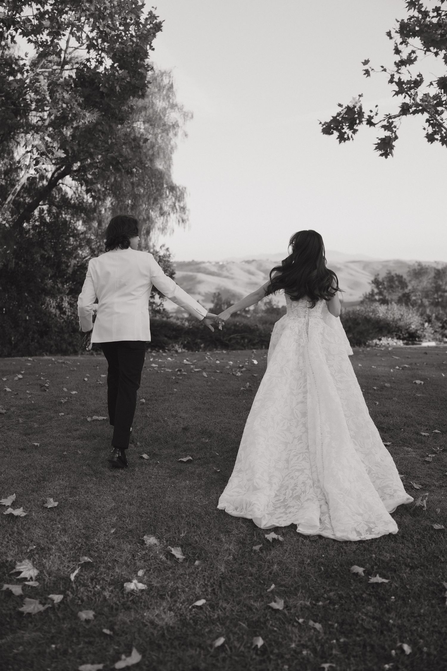 Black and white photo of bride and groom holding hands running through the grass.