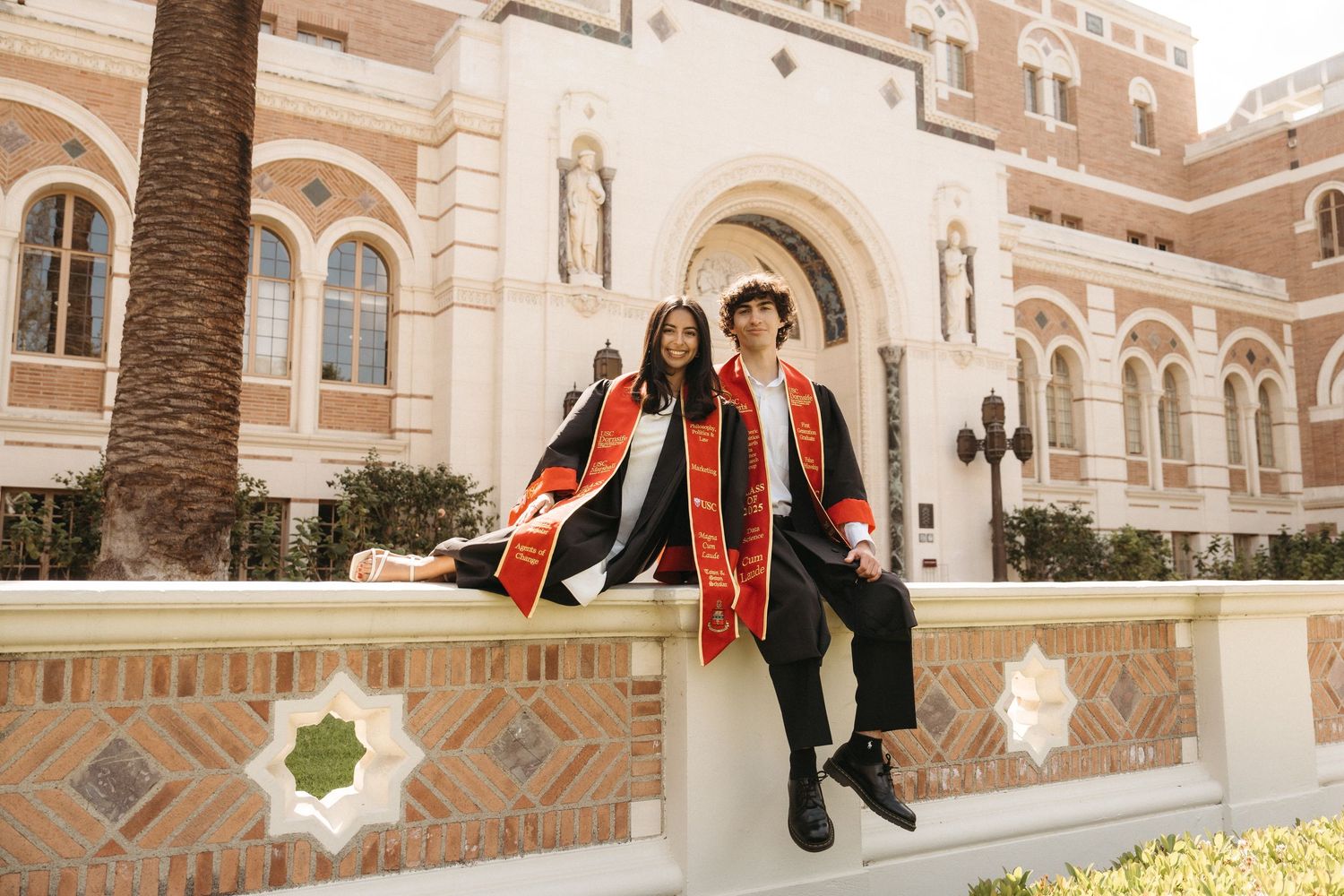 USC graduates posing in front of Doheny Memorial Library wearing their graduation gowns and stoles during graduation photography session.