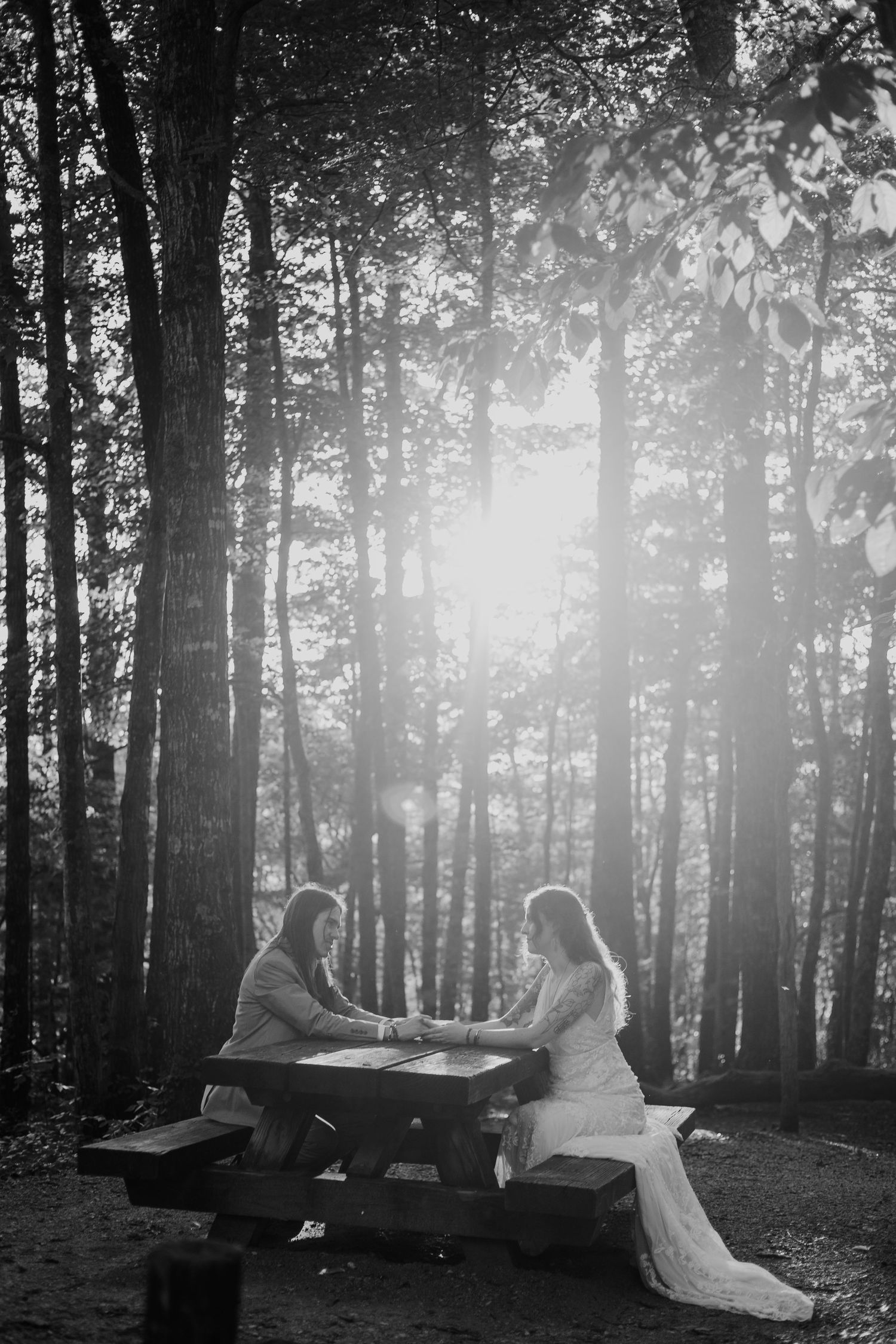 A black and white image of a couple sitting at a table in a forest setting.