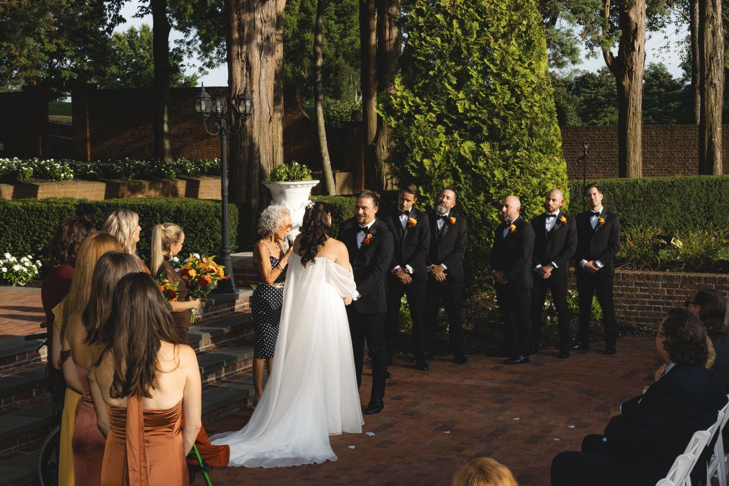 A bride and groom exchange vows during an outdoor wedding ceremony surrounded by wedding guests.