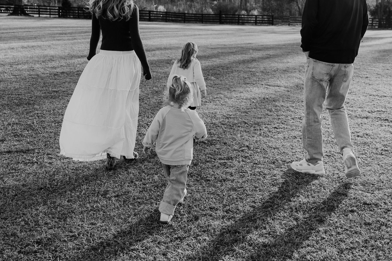 Black and white photo of a family walking across a grassy field, two parents with two young children.