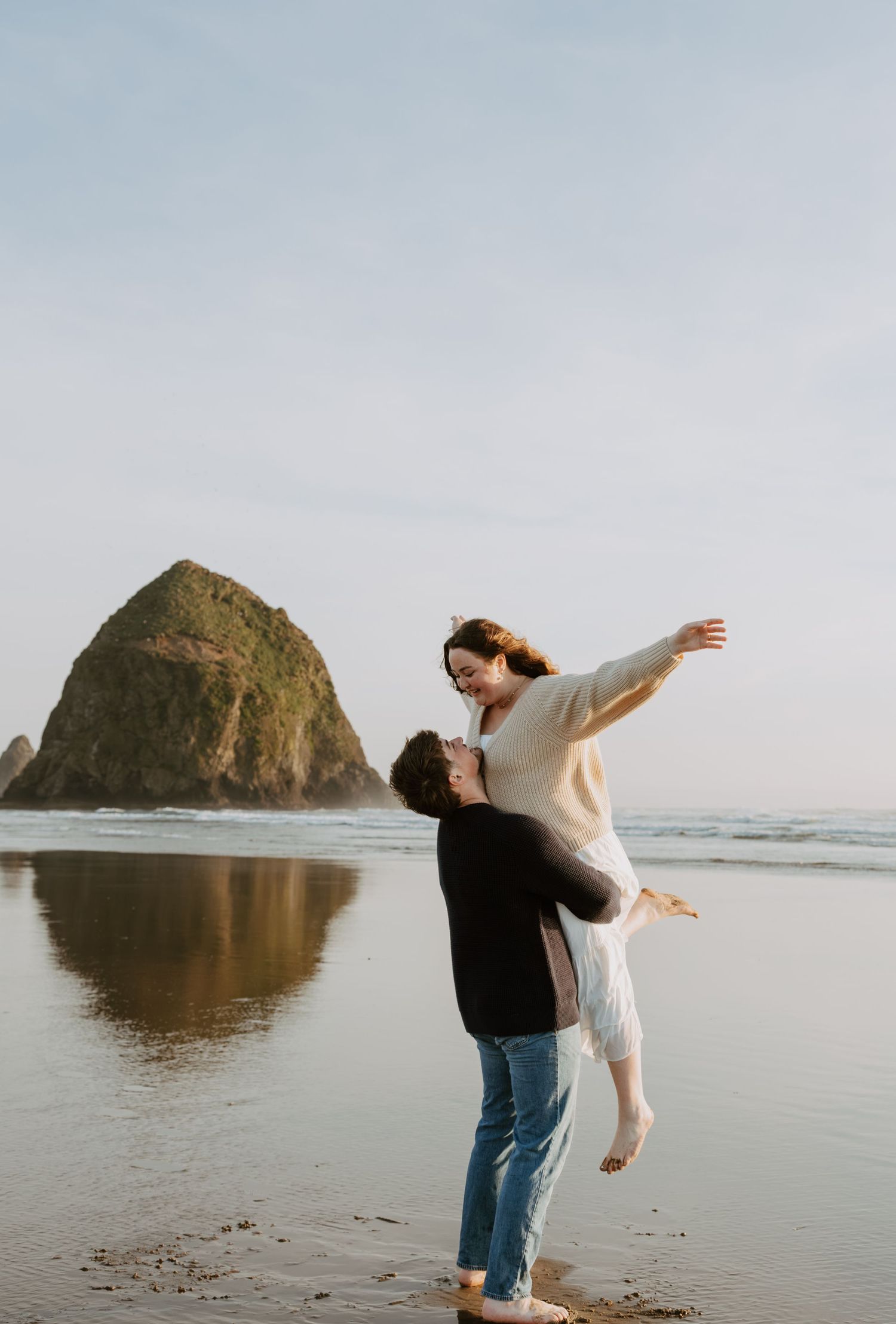 Couple sharing a joyful moment on the beach, man lifting woman near Haystack Rock at Cannon Beach, Oregon.