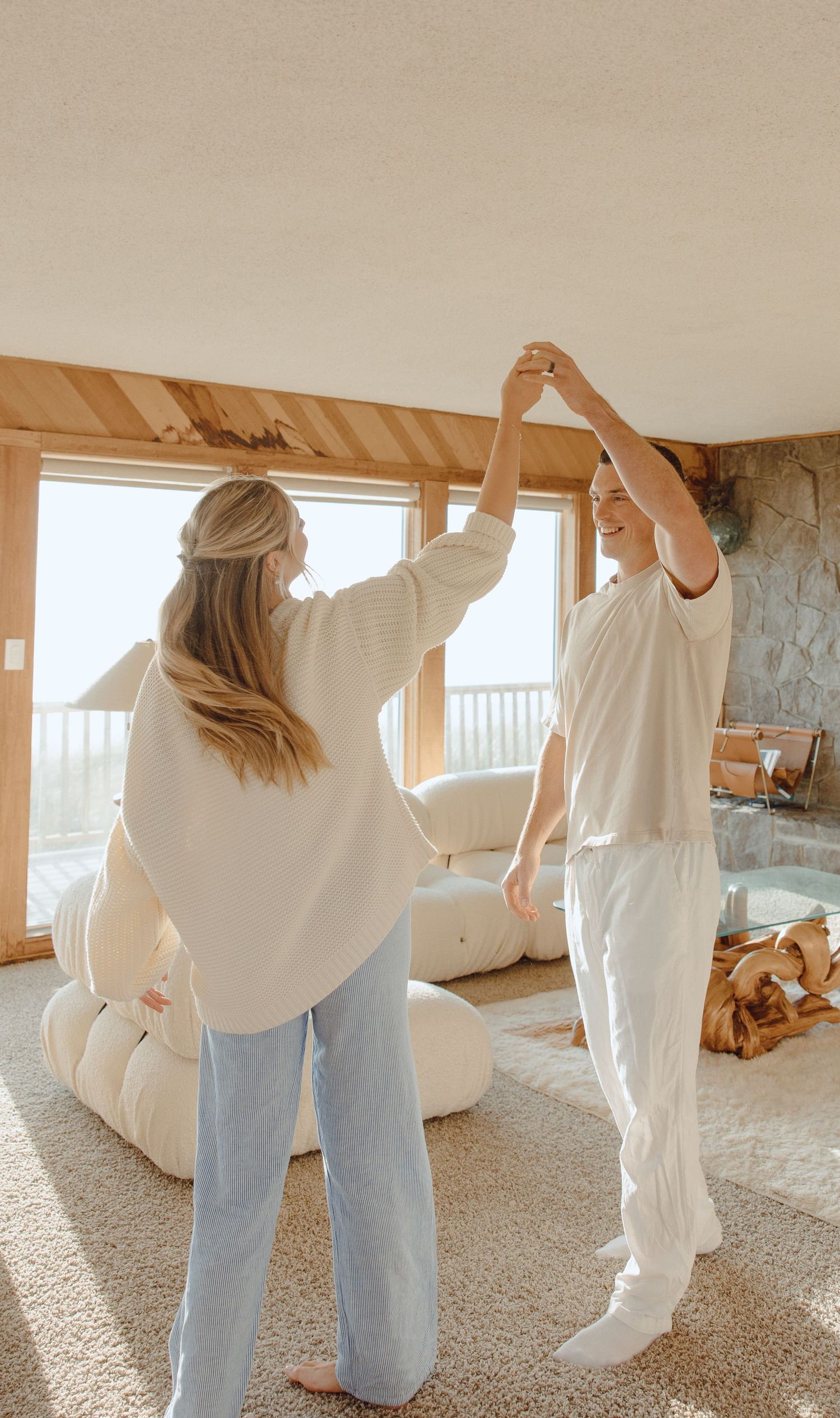 Couple dancing joyfully in a bright living room with large windows and ocean view.