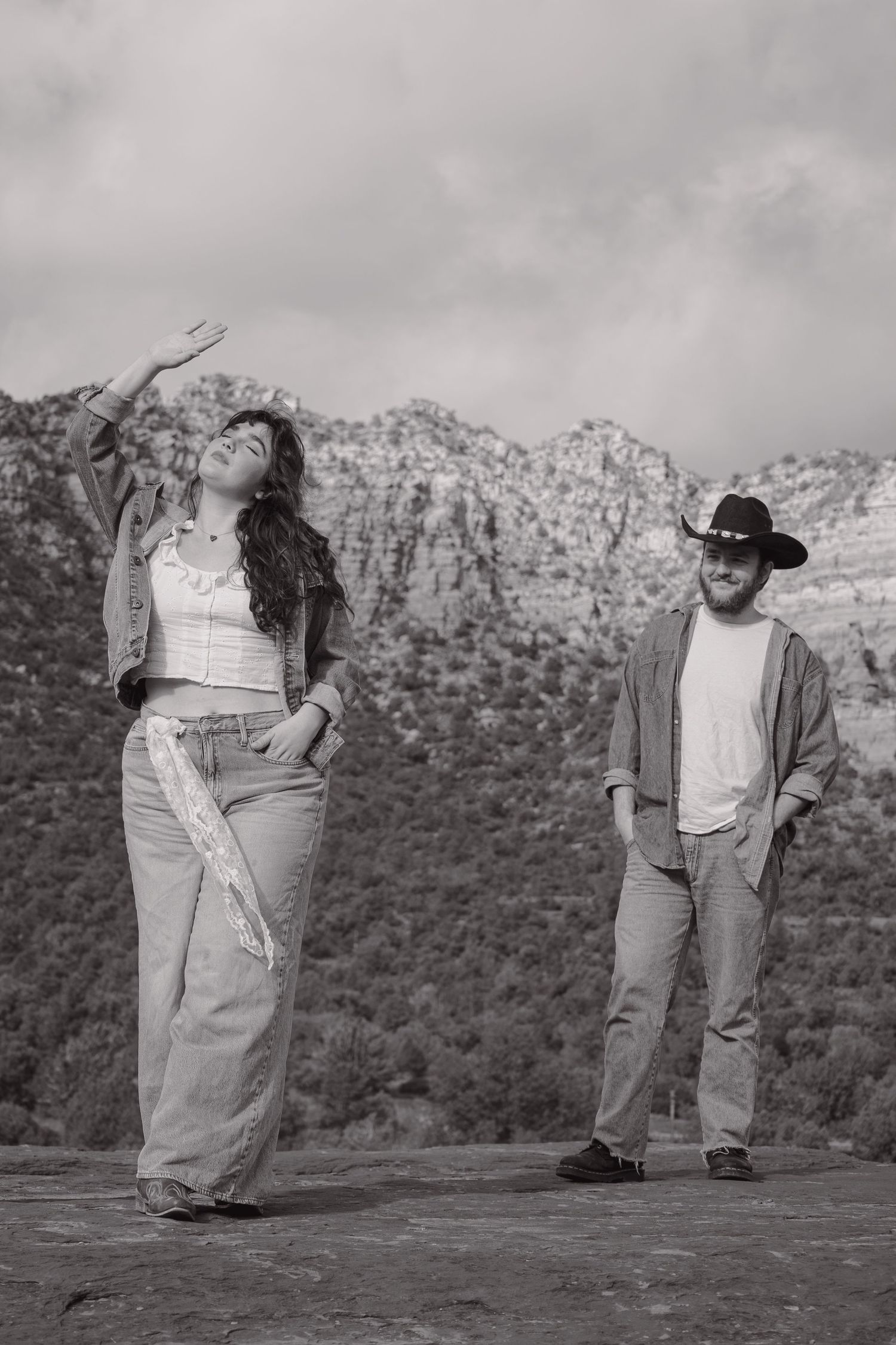 Black and white photo of a couple posing on a rock ledge with mountain landscape in Sedona.