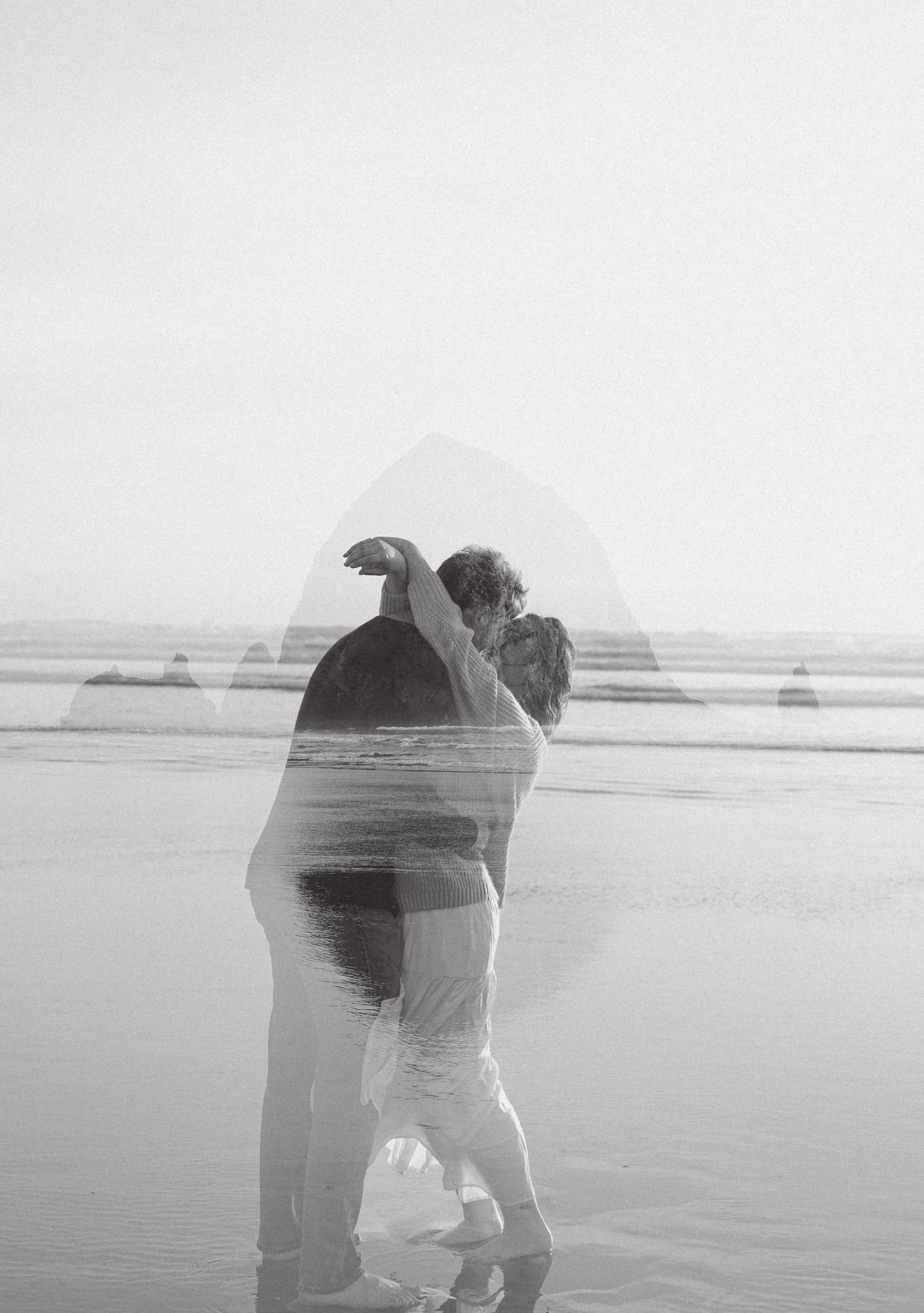 Black and white double exposure photo of a couple embracing on a misty beach shoreline.