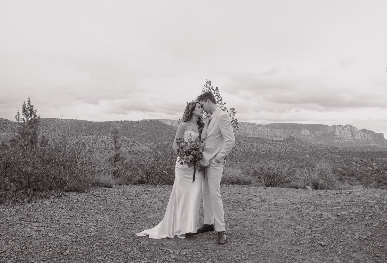 Black and white photo of bride and groom kissing on mountain overlook.