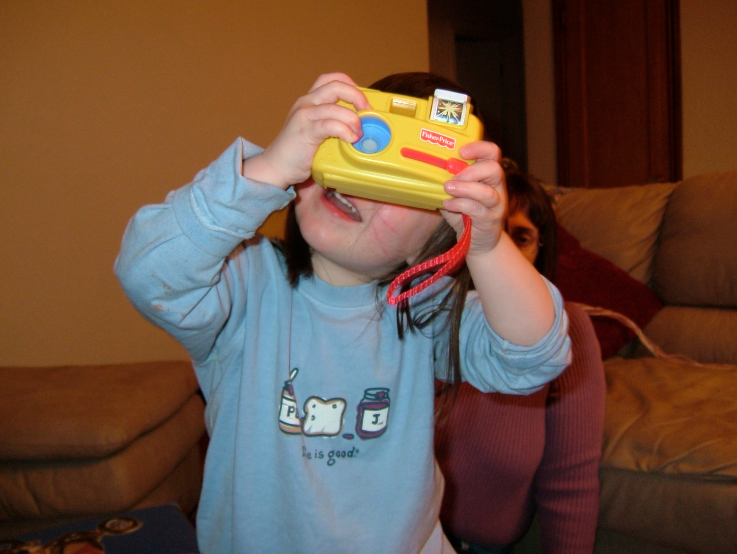 Young child holding yellow toy camera up to face indoors.