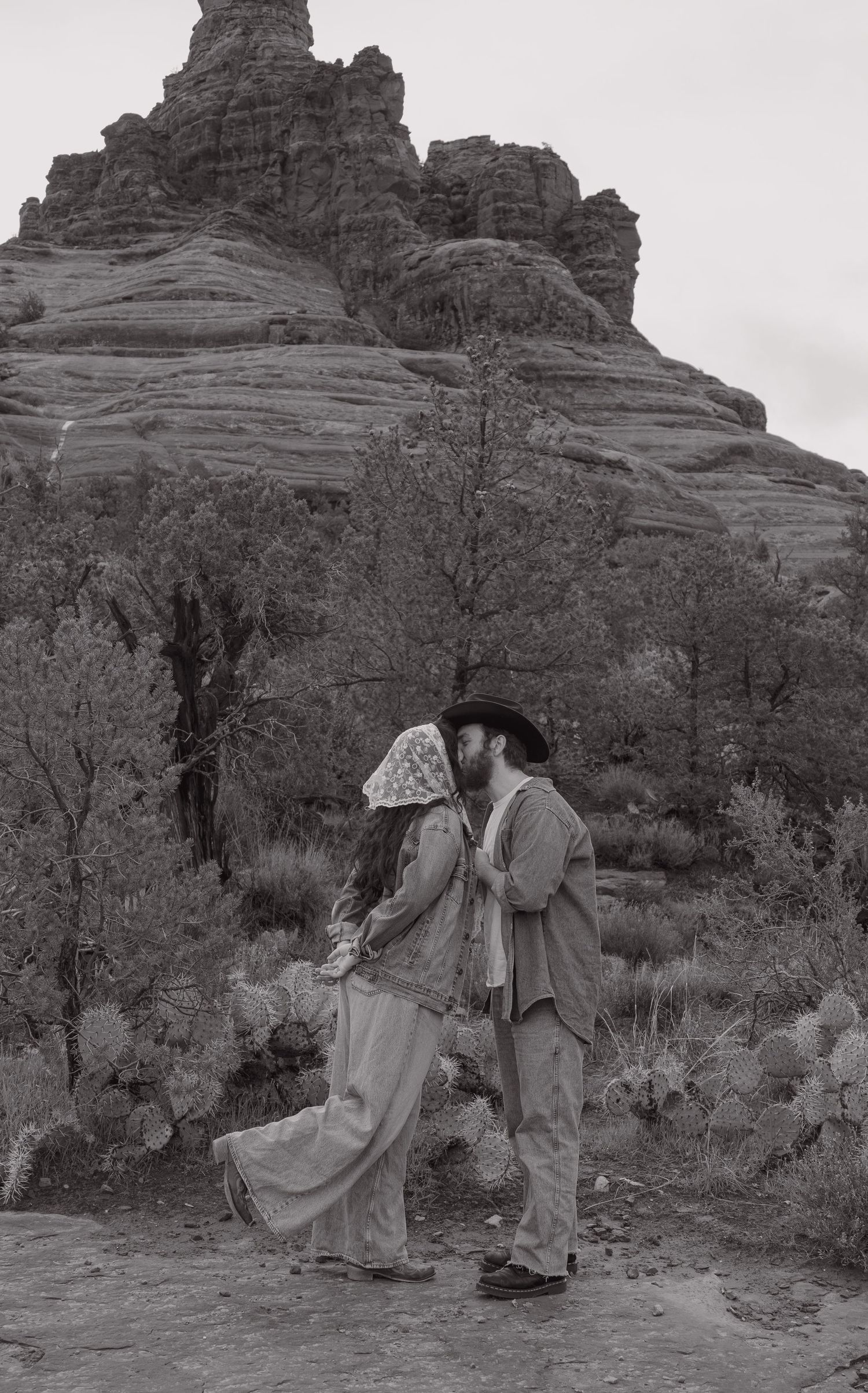 Black and white romantic photo of a couple kissing near red rock formations in Sedona, Arizona.