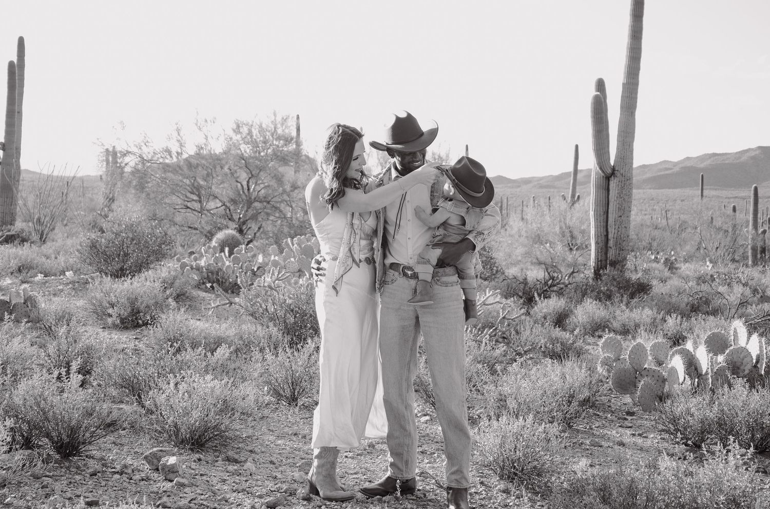 Black and white photo of couple dancing in desert landscape with saguaro cacti in the background.