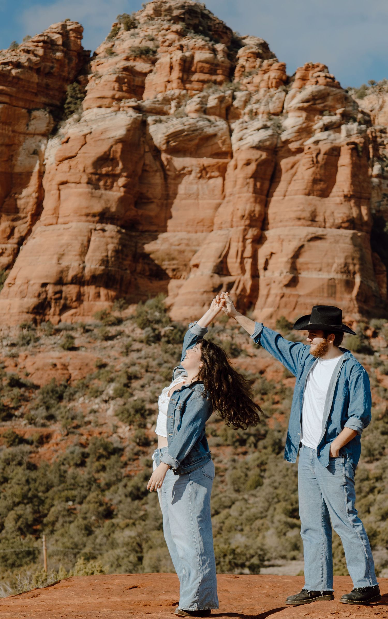 Couple dances together in front of stunning red rock formations in Sedona, Arizona on sunny day.