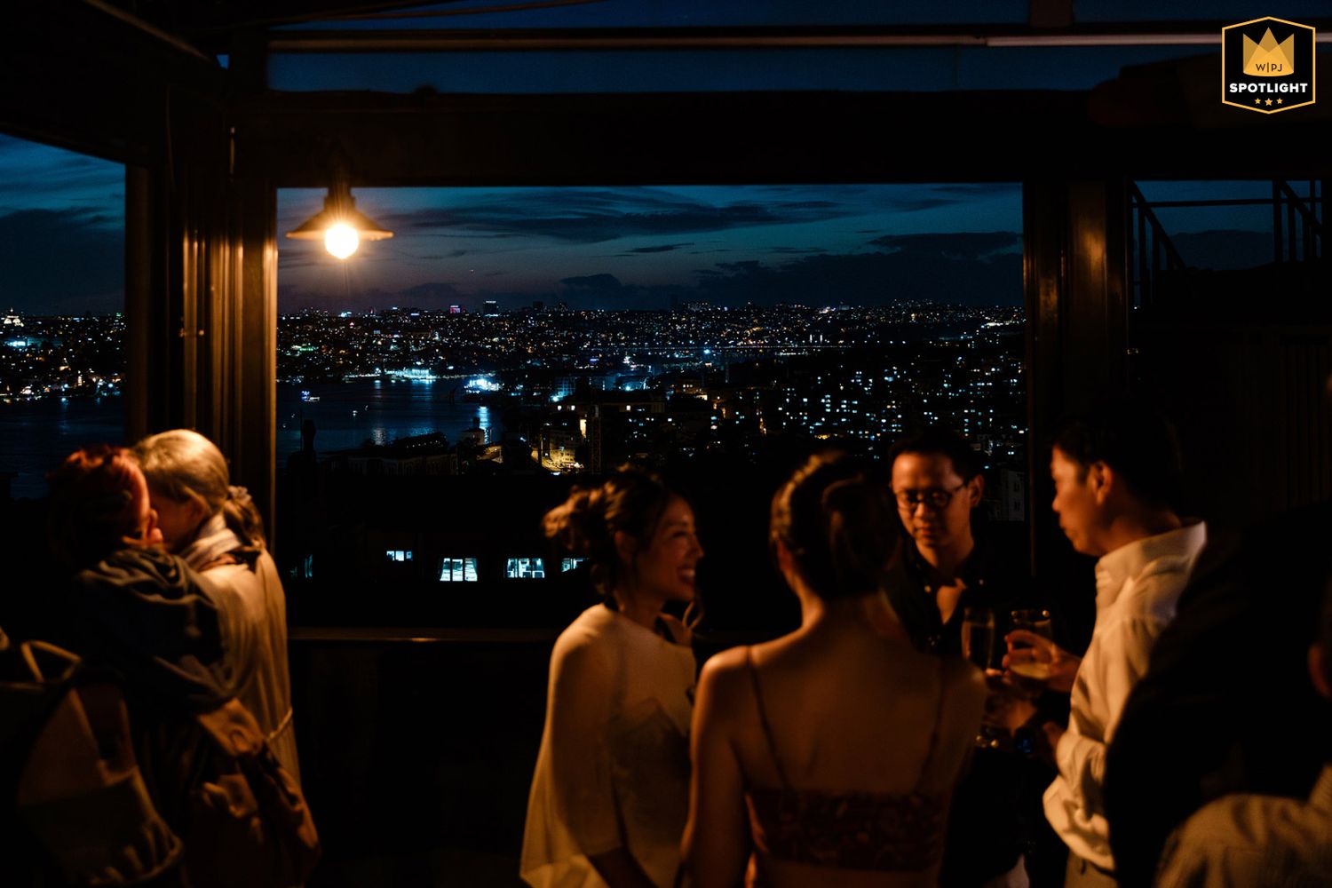 WPJA award-winning atmospheric photo of wedding guests talking in silhouette against the beautiful, illuminated night skyline of Istanbul.