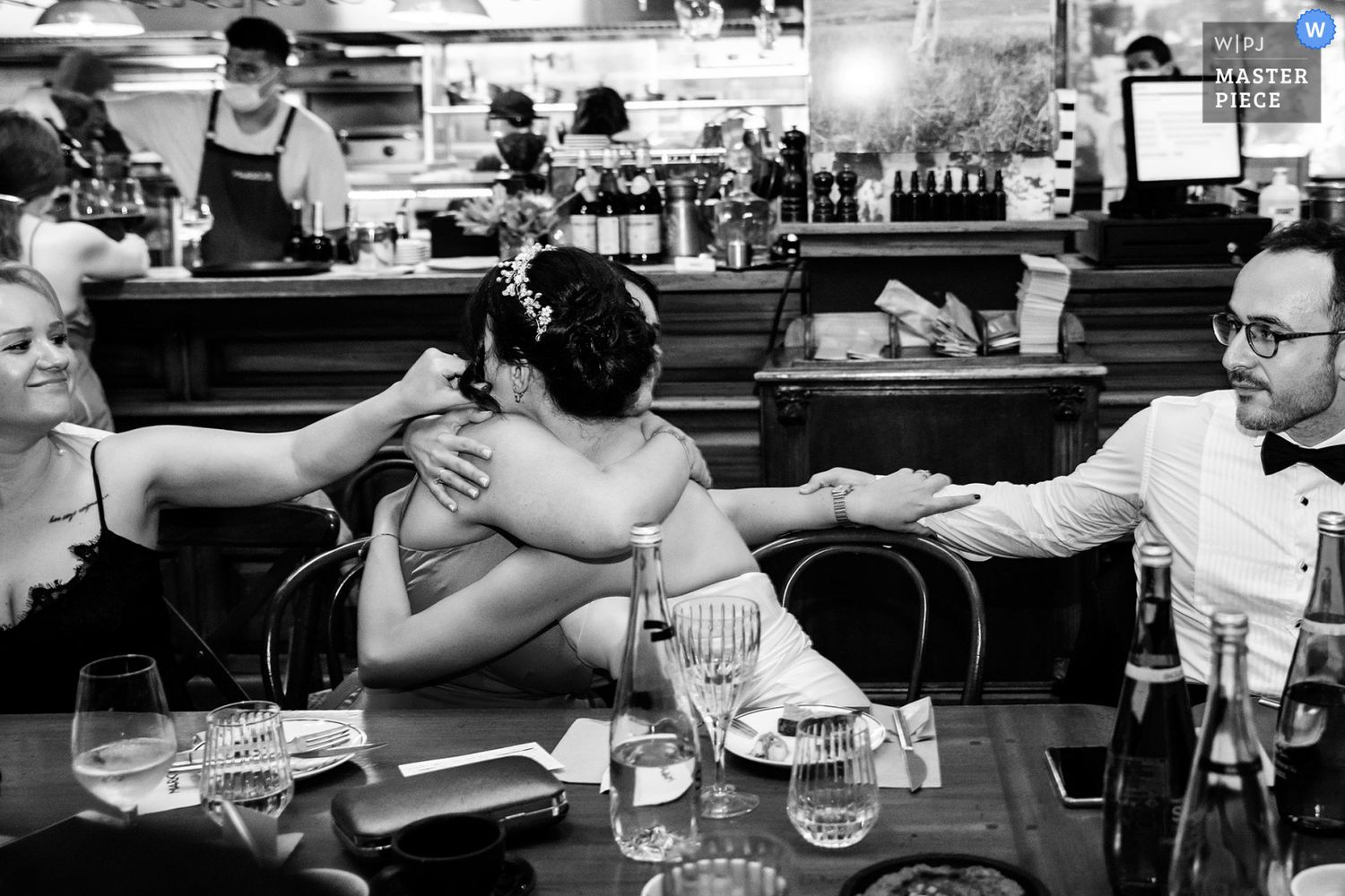 WPJA Masterpiece award-winning candid black and white photo of a bride sharing a deep, tight hug with a guest at the dinner table.
