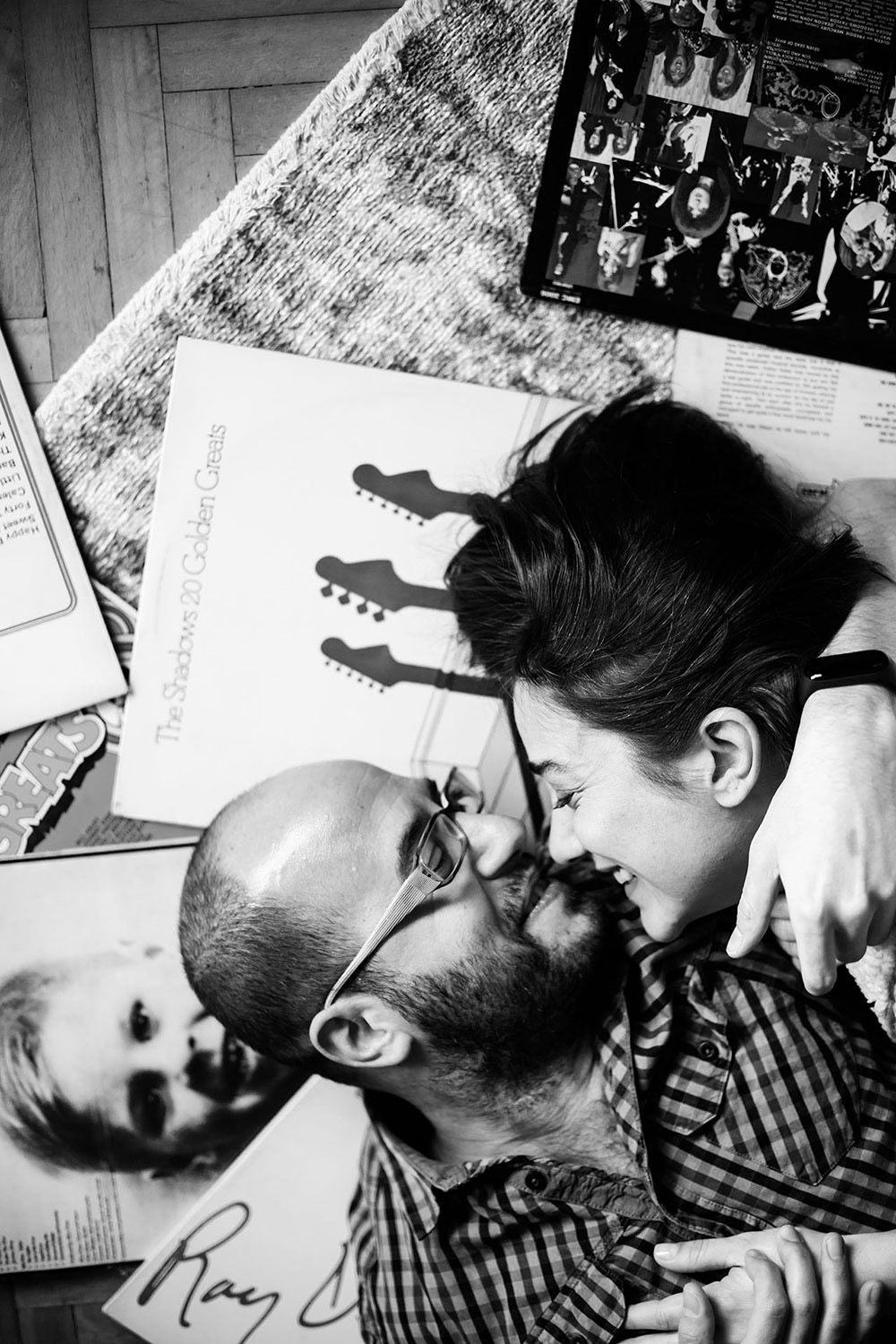 An intimate, at-home lifestyle couple session captured from above in black and white, showing a couple lying on a rug and smiling playfully
