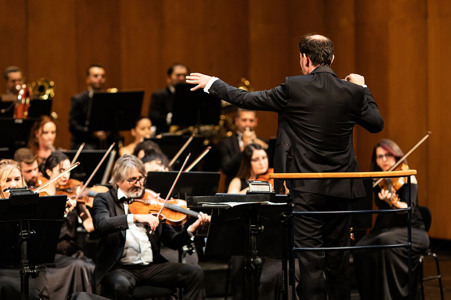 A conductor dynamically leading a live symphony orchestra during a grand corporate gala and cultural event.