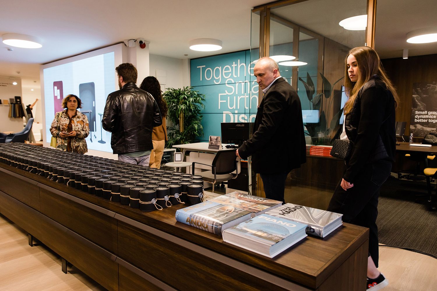 Corporate attendees walking past a long display table lined with branded gift boxes and architecture books at a design showroom event.