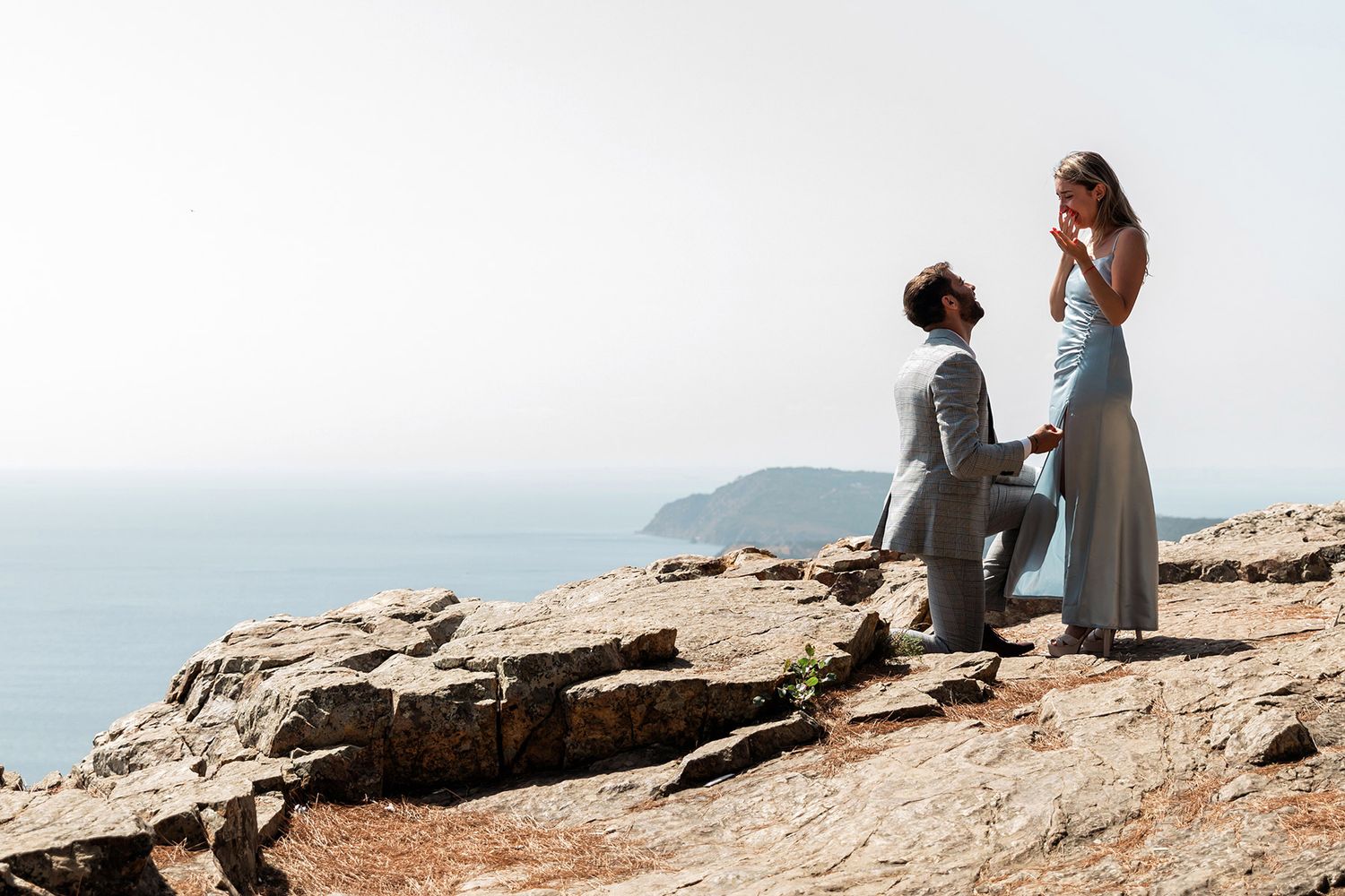 A man kneels for a surprise cliffside proposal to his emotional fiancé overlooking the ocean on Büyükada Island, Istanbul.