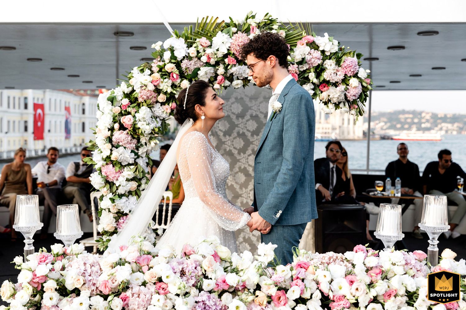 WPJA award-winning portrait of a bride and groom holding hands at a lavish floral altar during a Bosphorus boat wedding in Istanbul.