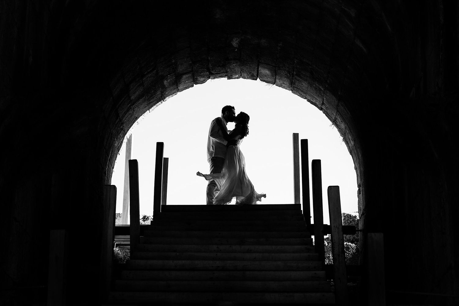Dramatic black and white silhouette of a bride and groom kissing under a massive stone archway at the ancient Kaunos ruins.