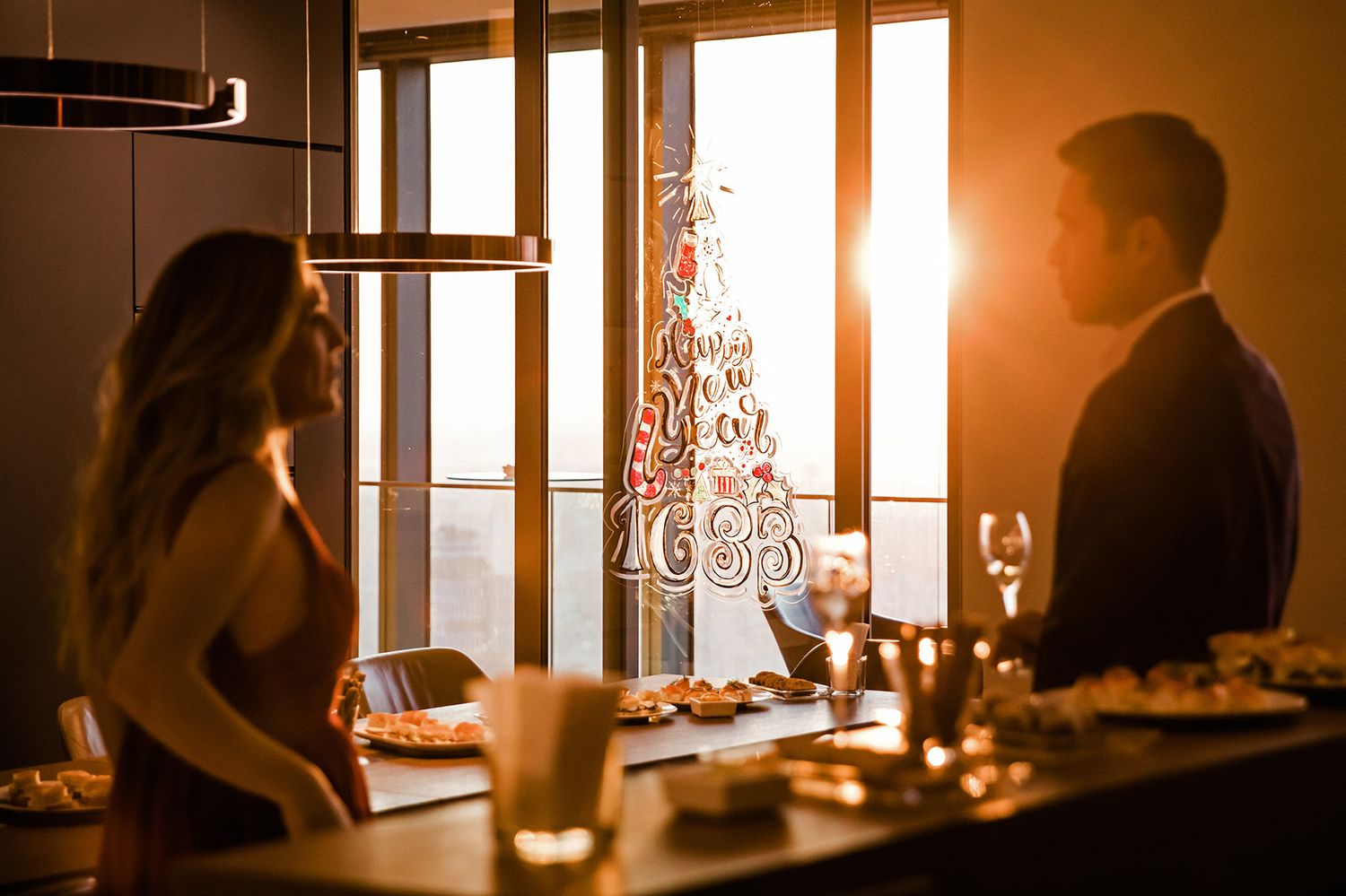 Silhouetted guests networking at a sunset corporate holiday party featuring a Happy New Year window decal.