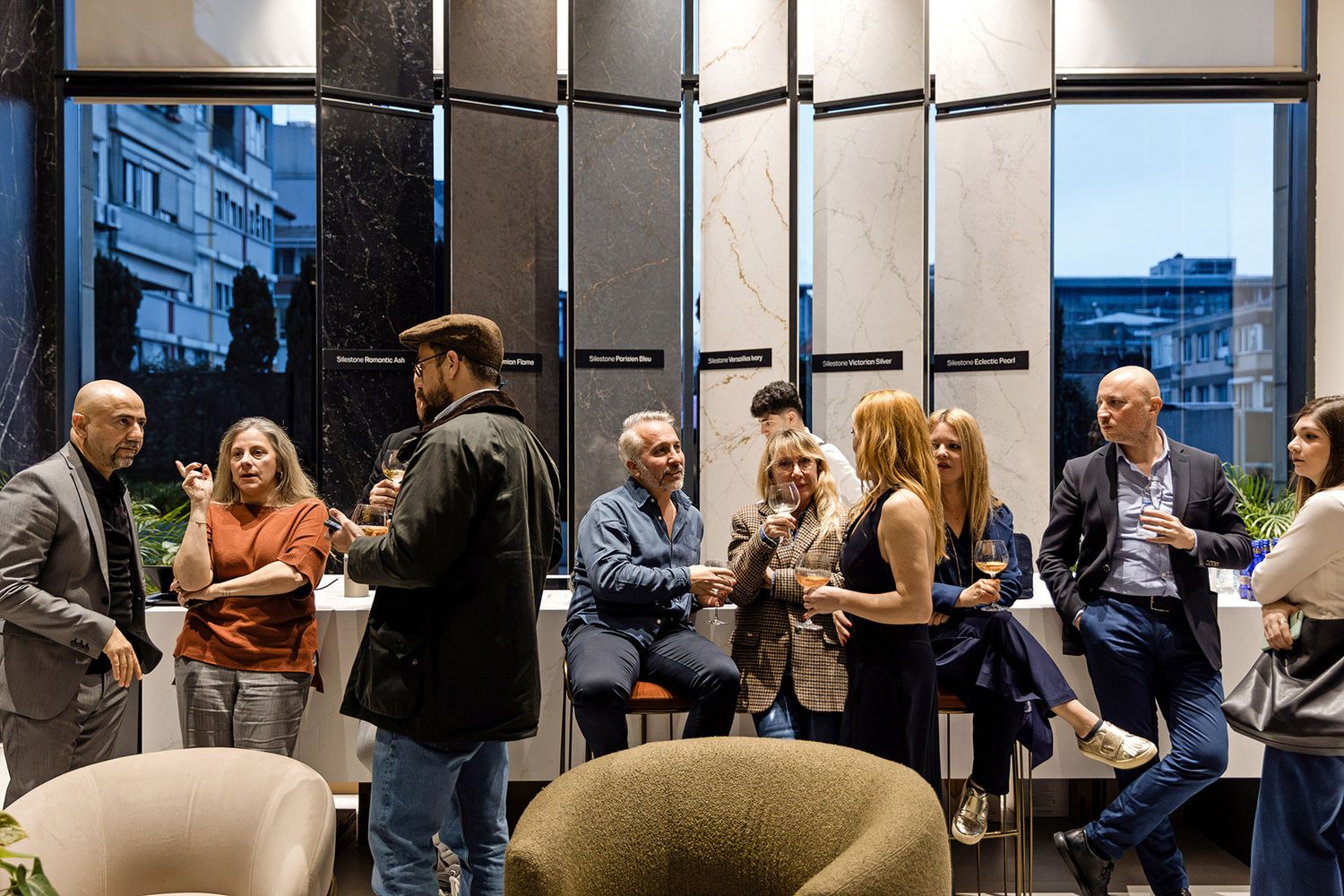 Professional guests networking and holding wine glasses in front of large, elegant stone surface displays at an architectural showroom event