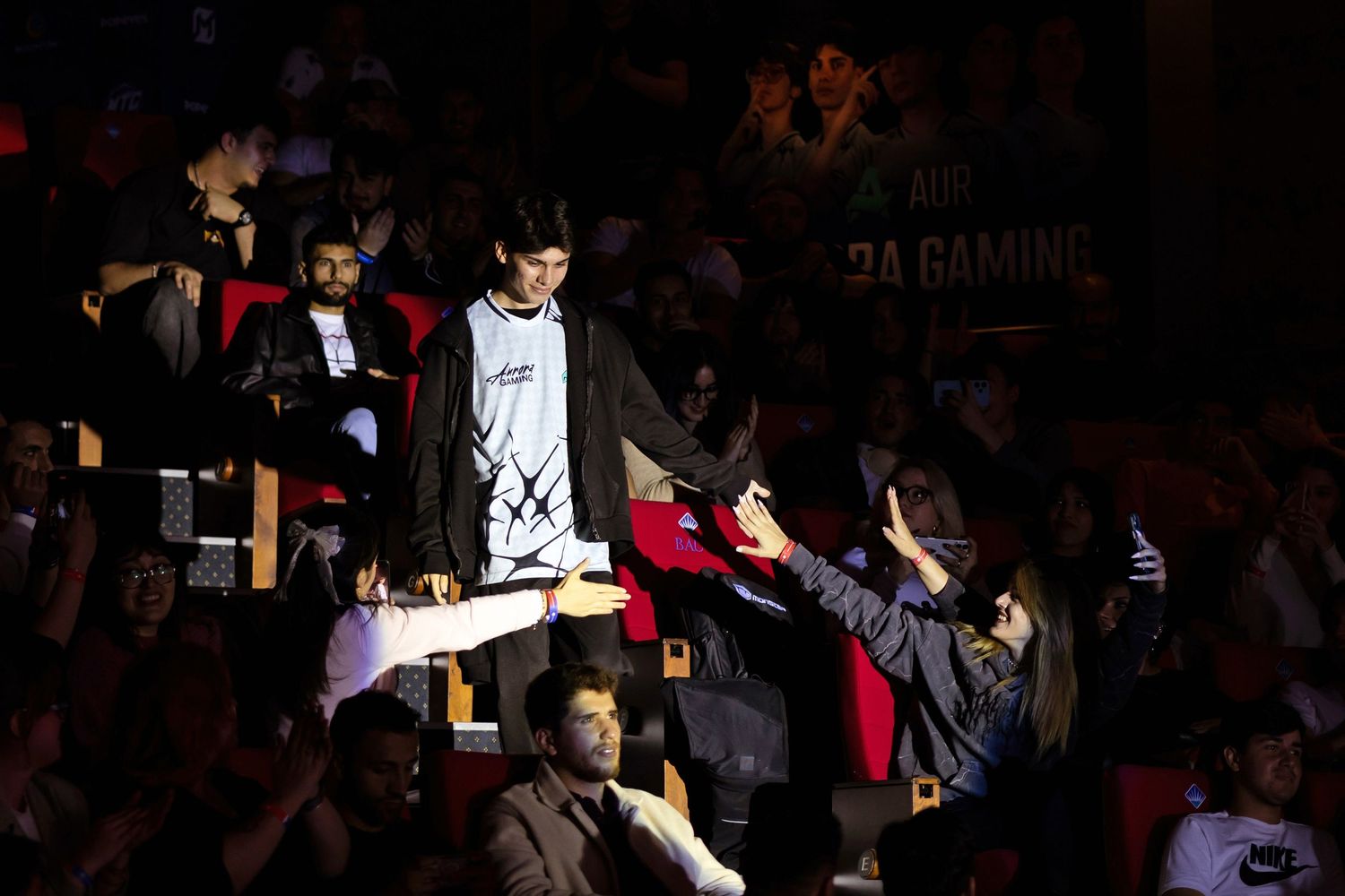 A professional esports player high-fiving excited fans in the audience while walking toward the main tournament stage.