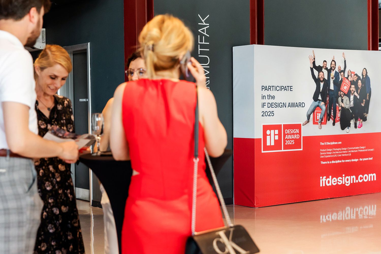 Corporate guests networking and mingling in front of a brightly lit, branded iF Design Award step-and-repeat backdrop.