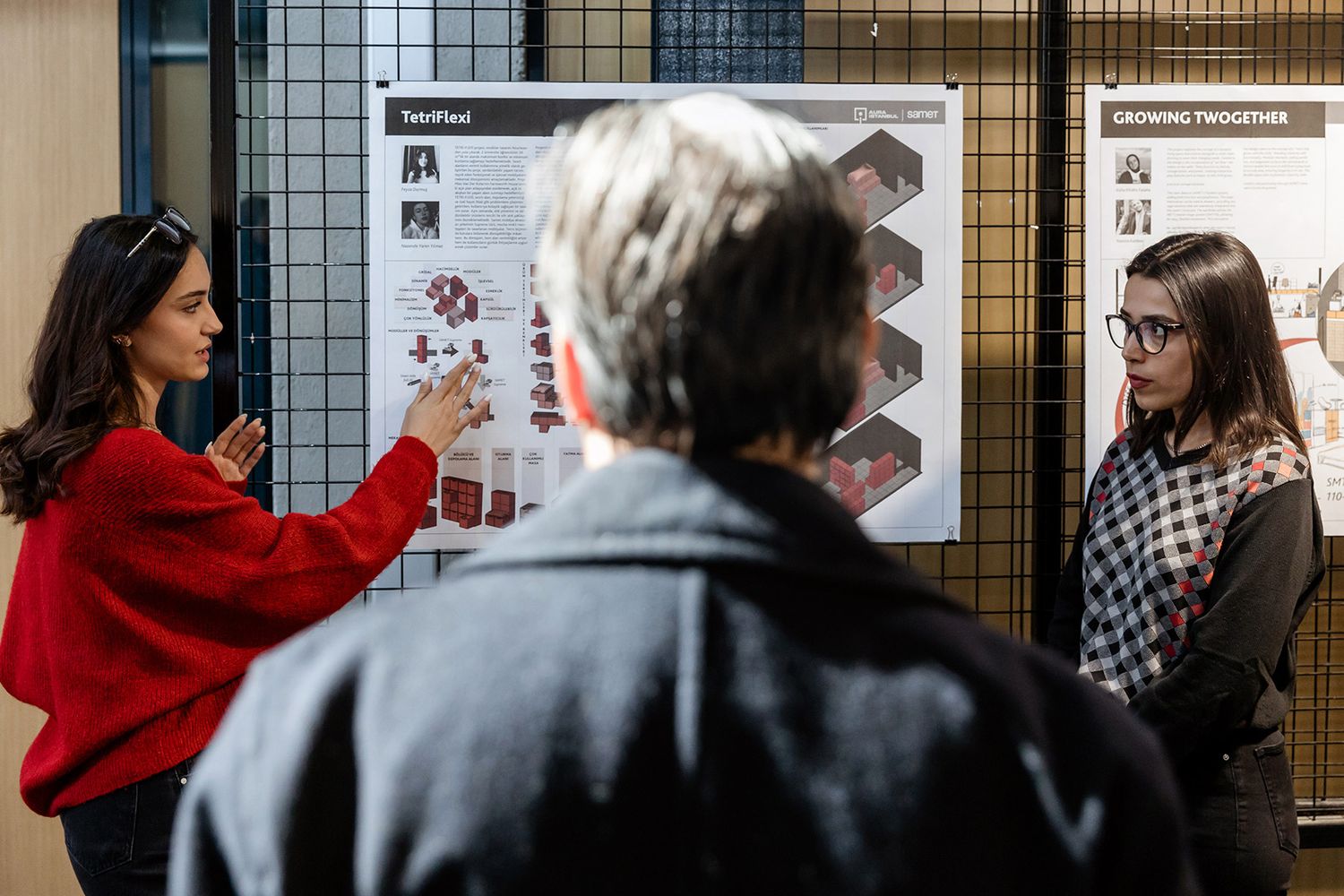 A young female architecture student confidently pitching her design project to evaluators at a corporate academic exhibition.