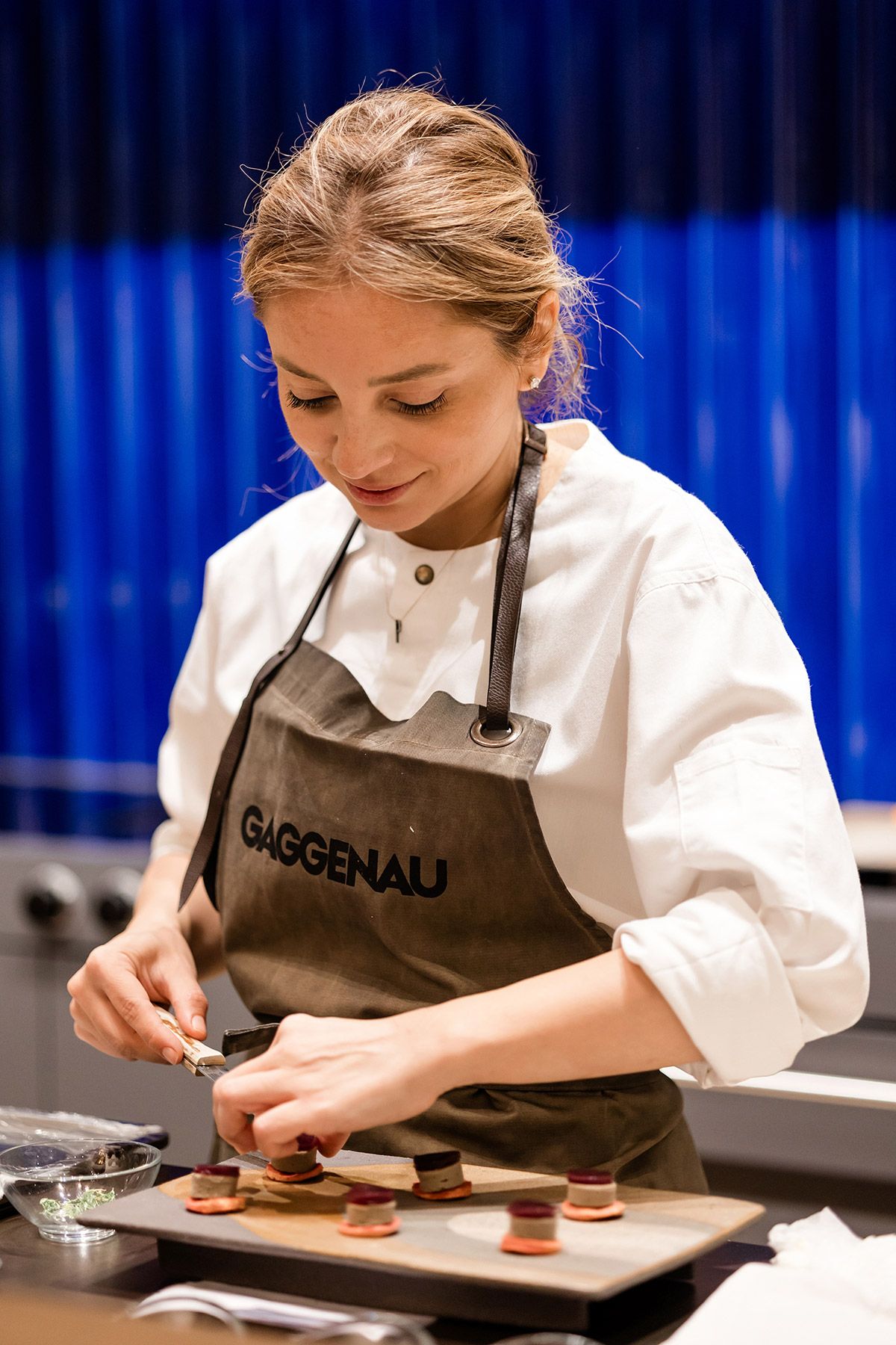 Chef Pınar smiling and meticulously plating gourmet appetizers while wearing a branded apron during a Gaggenau culinary corporate event.