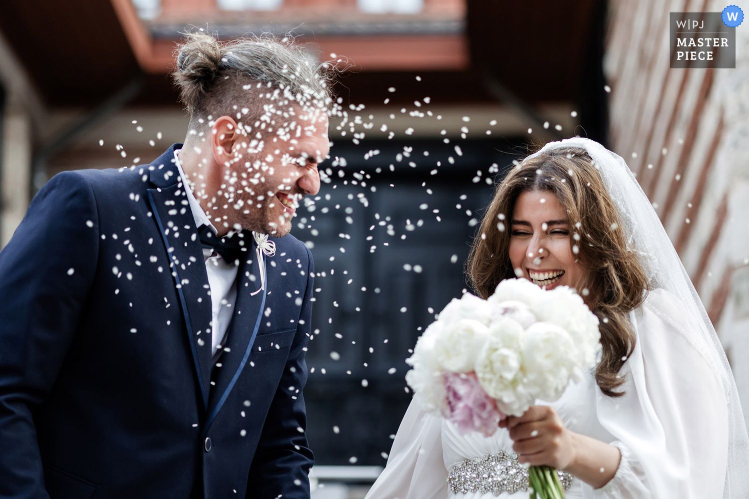 WPJA award-winning candid shot of a joyful bride and groom laughing hard while being showered with rice during their wedding exit.