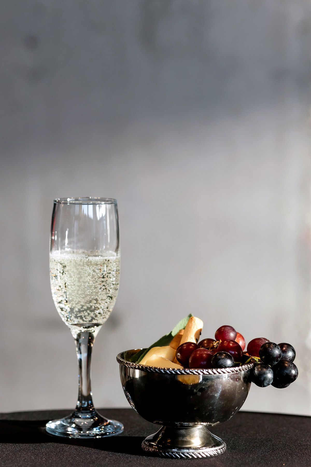 Close-up of a filled champagne flute and a silver bowl of gourmet grapes and cheese at a luxury corporate event.