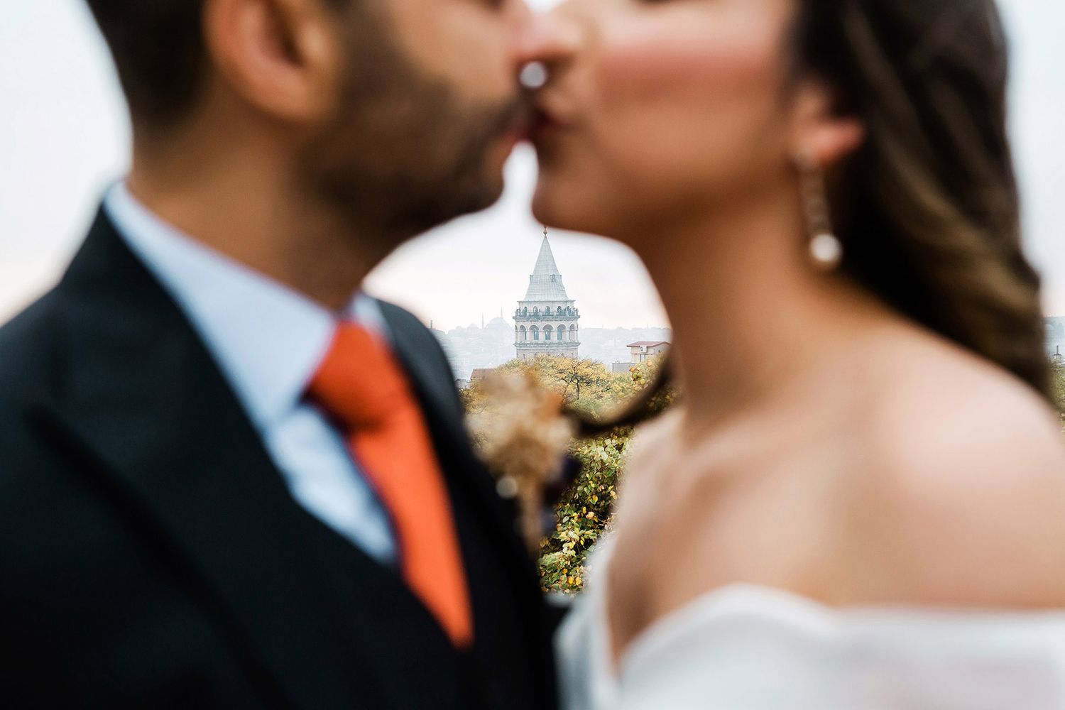 Creative out-of-focus shot of a bride and groom kissing, perfectly framing the iconic Galata Tower in the background in Istanbul.