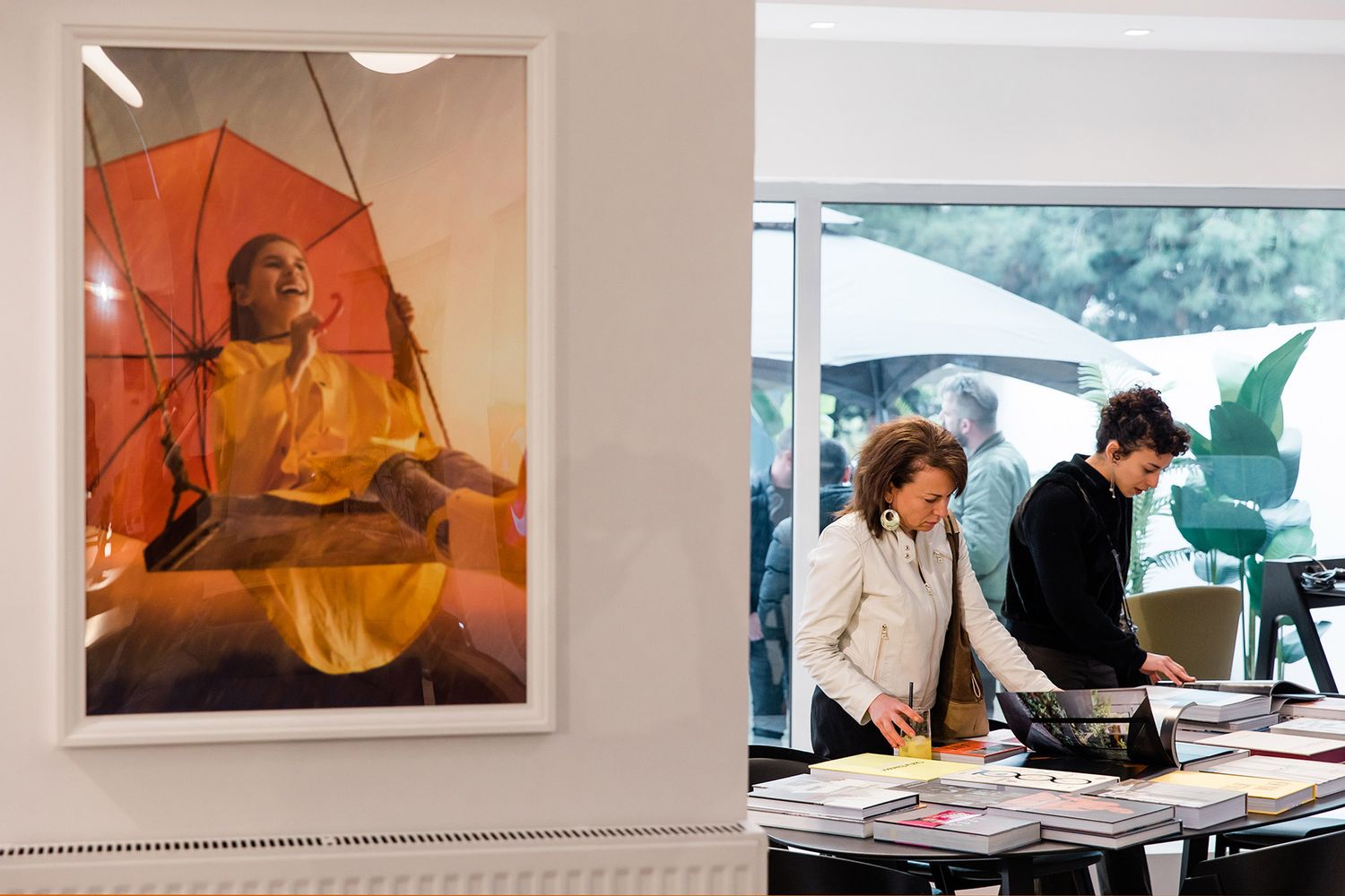 Two female event attendees browsing through a curated selection of design books at an upscale corporate exhibition and networking event.