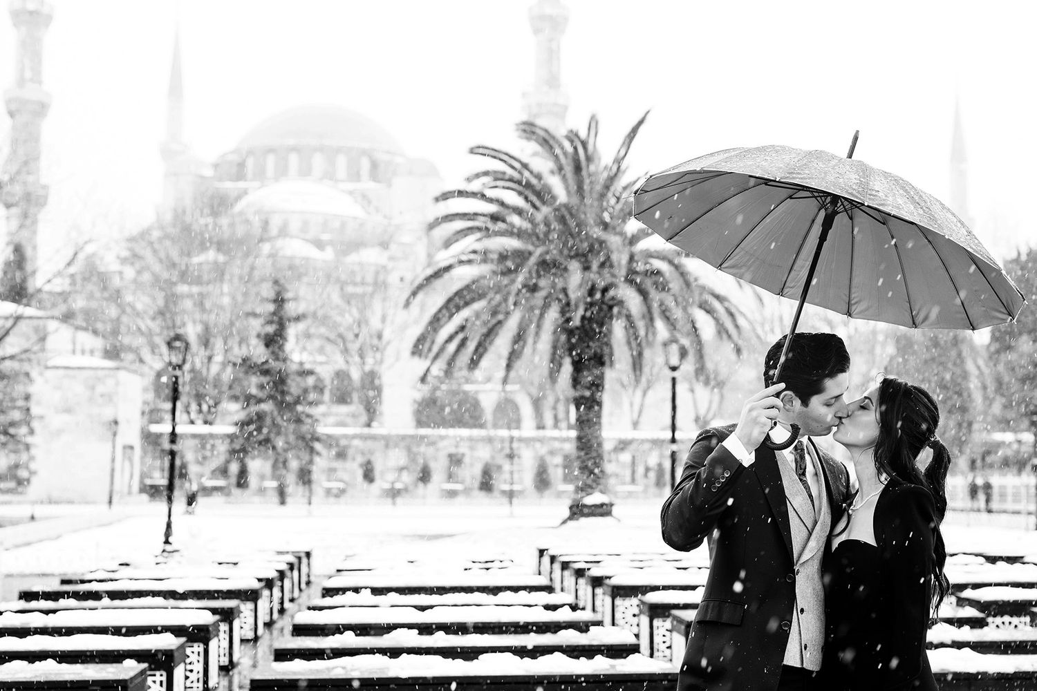 A romantic black and white portrait of a couple kissing under an umbrella during a snowy winter elopement at the Blue Mosque in Istanbul.