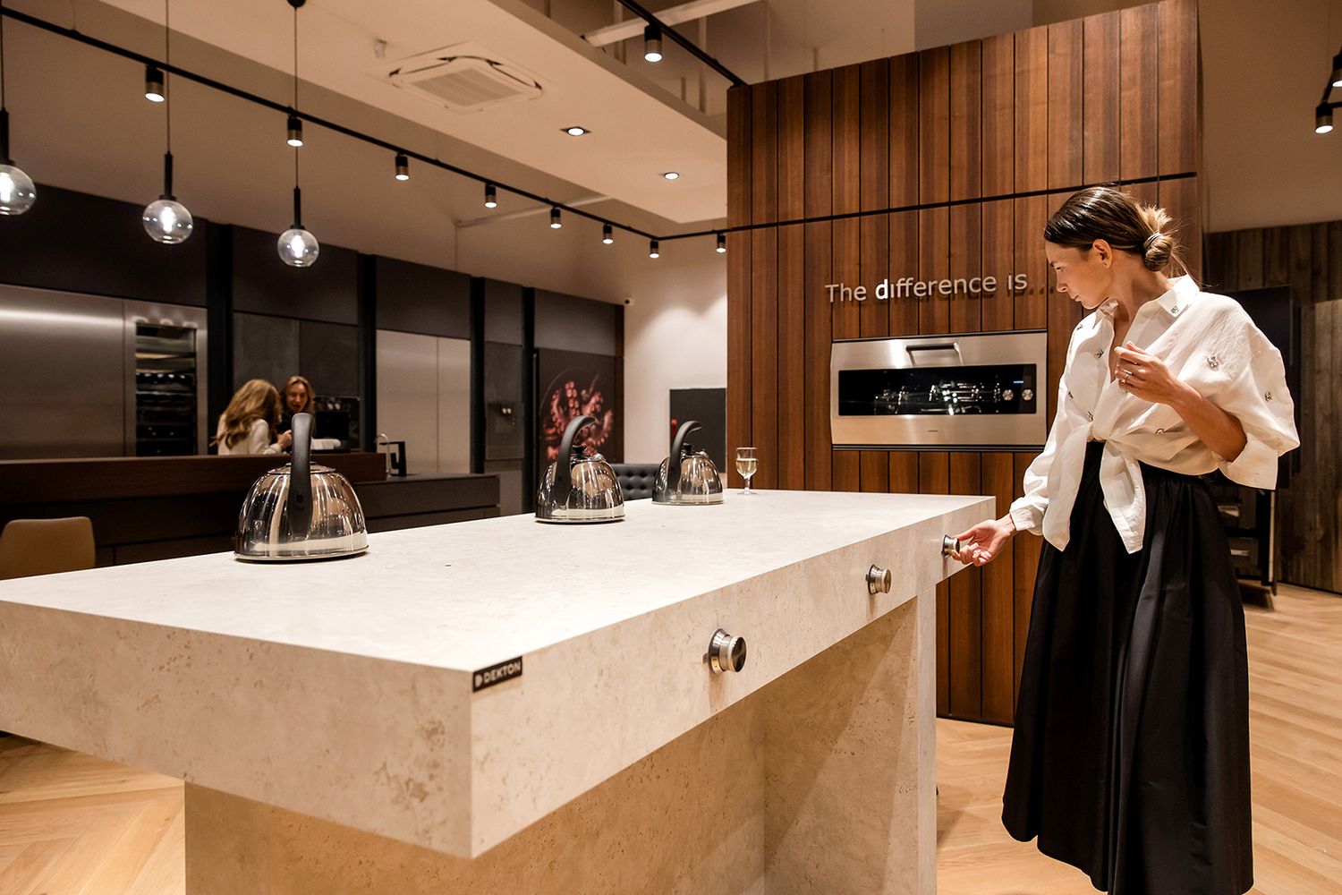A female guest interacting with modern kitchen appliances at a sleek, high-end corporate showroom event.