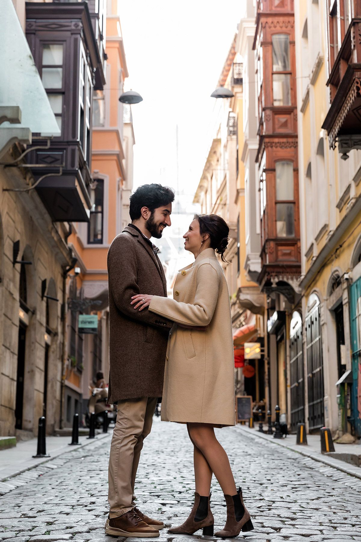 A smiling couple embraces while standing on a charming, historic cobblestone street in the Galata neighborhood of Istanbul.