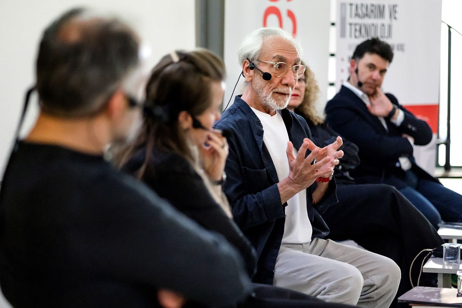 A male expert panelist using hand gestures to passionately explain a point during a design and technology seminar.