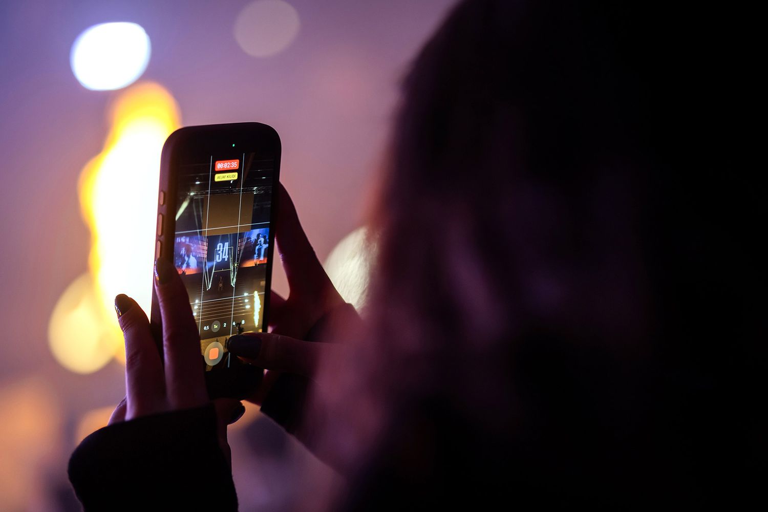 Close-up over the shoulder of an attendee recording massive stage pyrotechnics on a smartphone during an esports event.