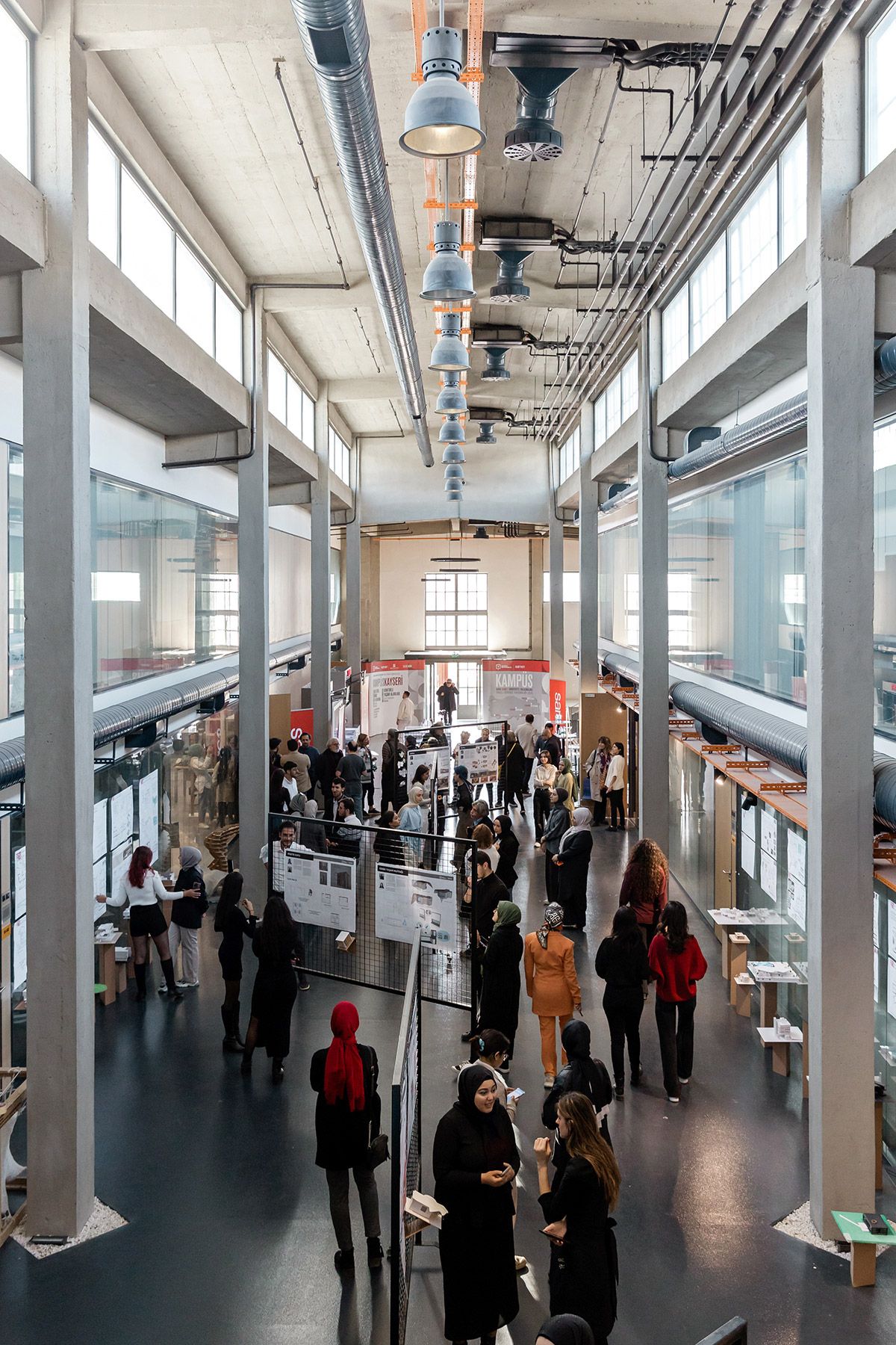 A high-angle, wide shot of attendees browsing architectural presentations and networking in a massive industrial exhibition hall.