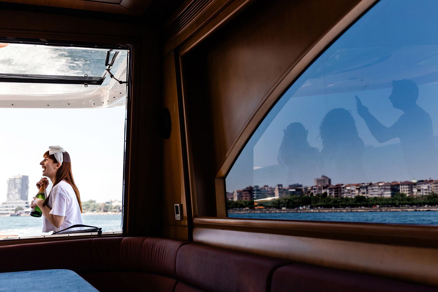 Smiling bride with champagne on a boat heading to Esma Sultan, guests reflected in the glass during a Bosphorus wedding in Istanbul.