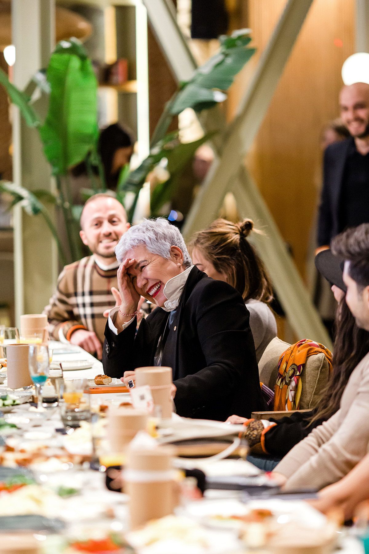 A female corporate guest laughing joyfully at a long dining table during a professional networking and brand event.