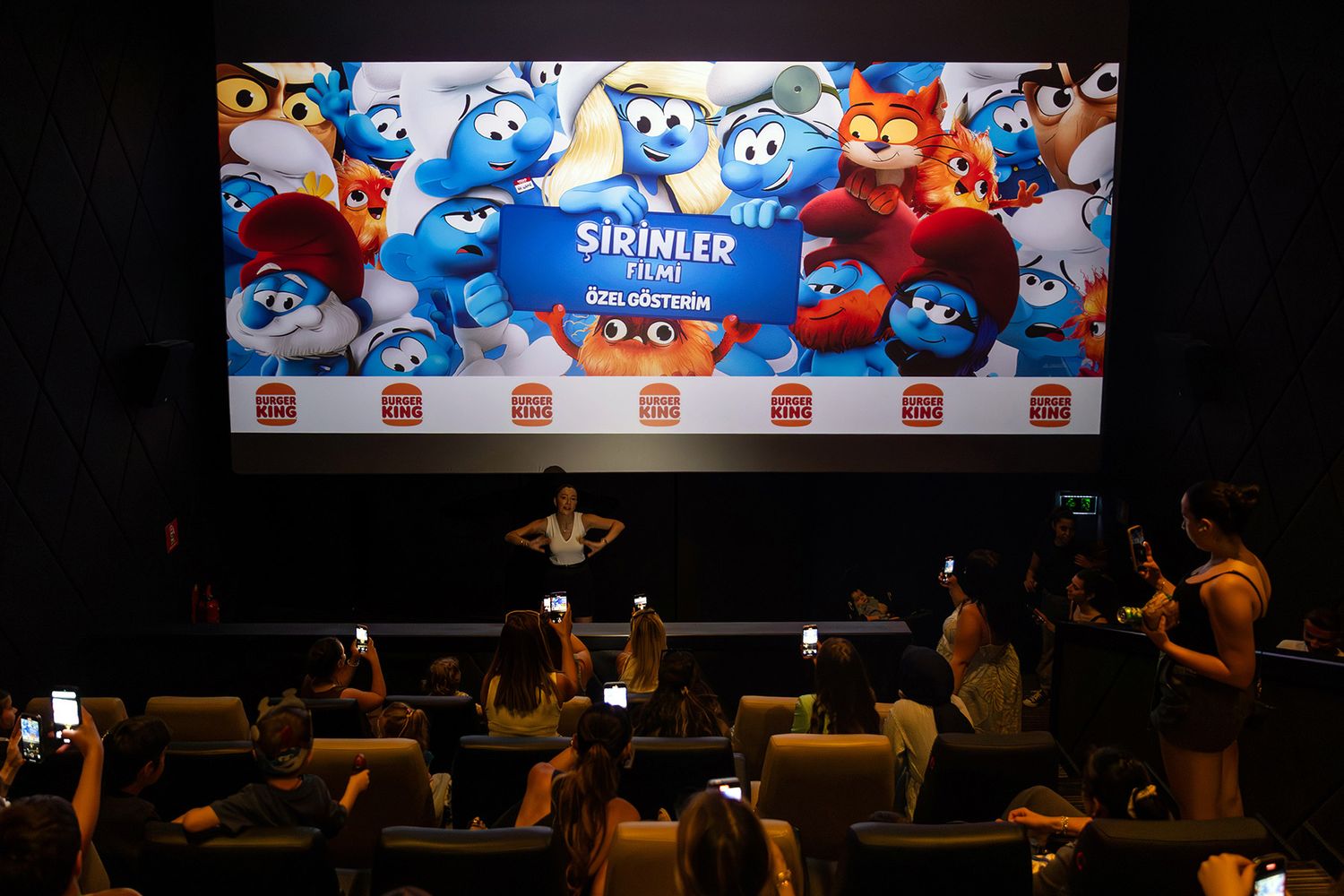 Event attendees taking smartphone photos of a presenter on stage before a private, Burger King sponsored movie screening.