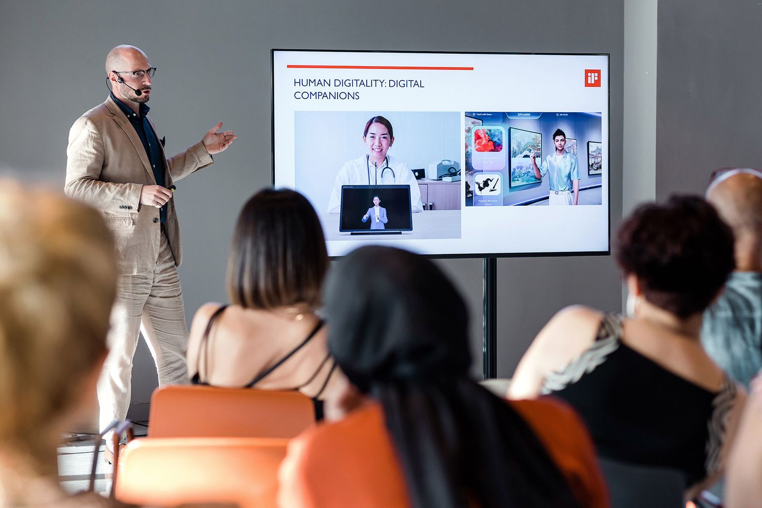A male keynote speaker delivering a presentation on digital companions and design to a seated audience at a corporate seminar.