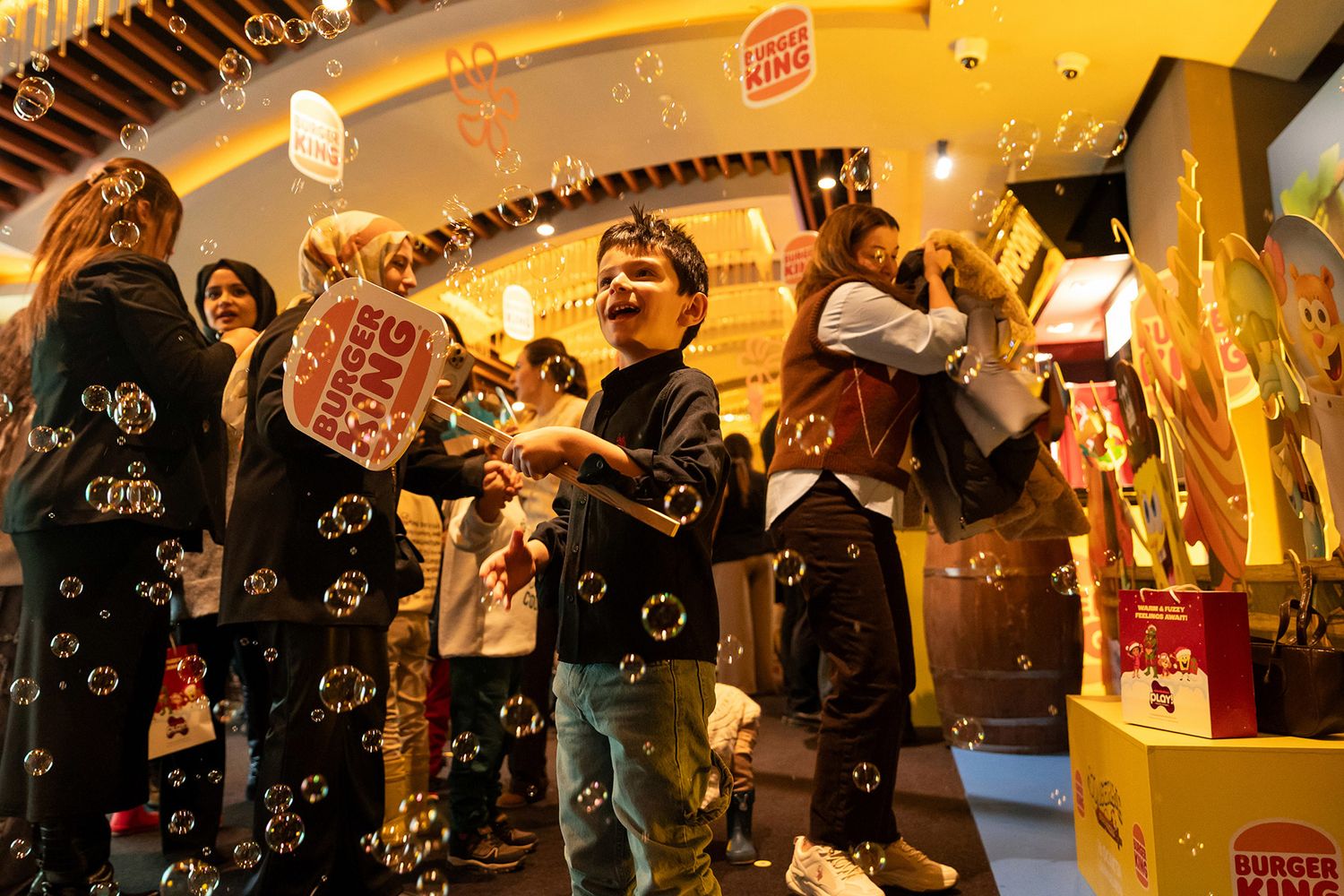 A young boy laughing joyfully while holding a Burger King sign amidst a shower of bubbles at a fun corporate brand activation.