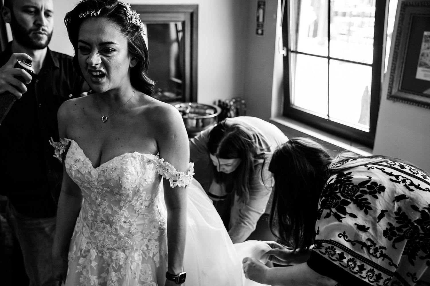 A bride makes a funny ouch face while getting her hair sprayed and dress adjusted during wedding prep at Koç Museum in Istanbul.