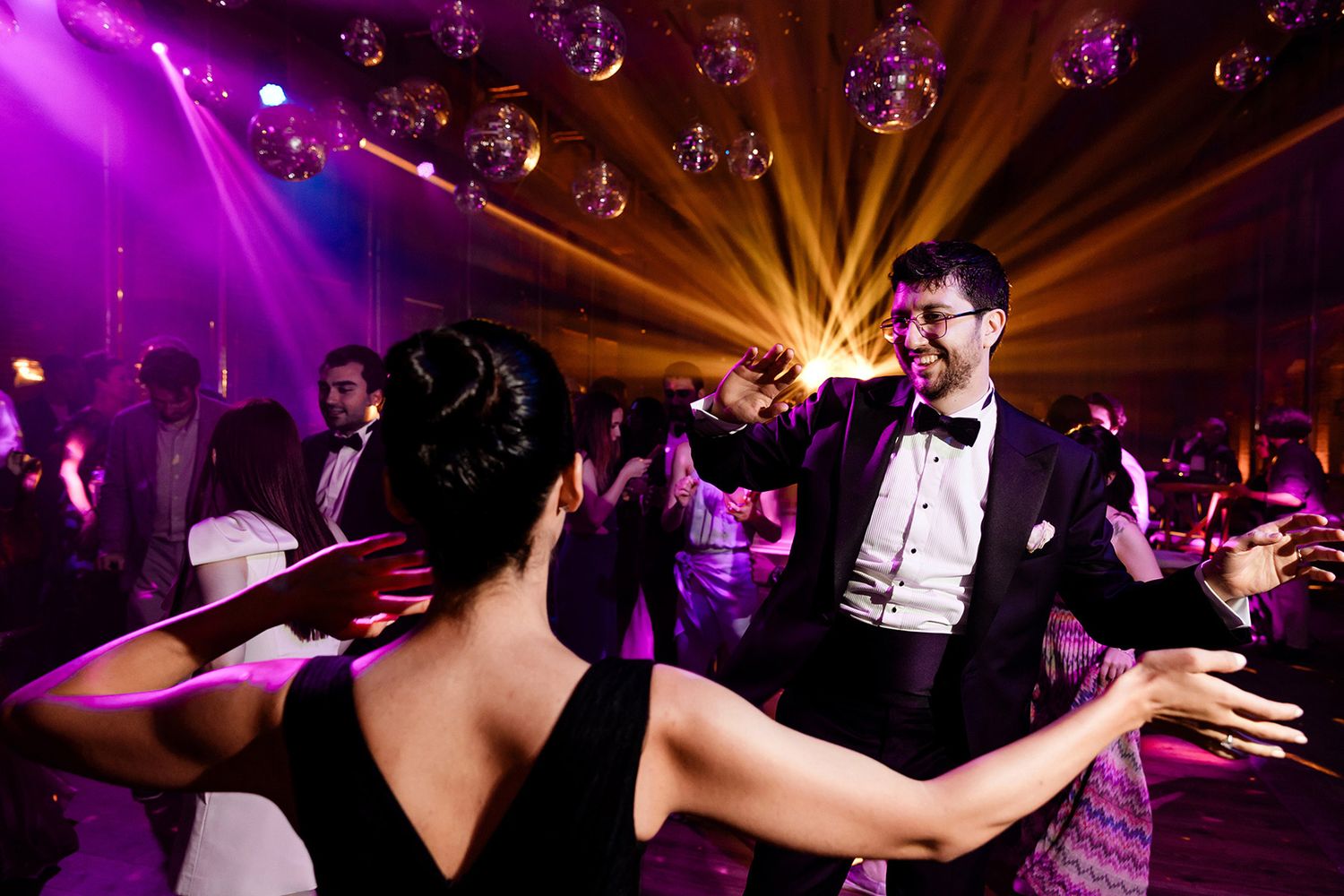 A groom dances enthusiastically with his sister under disco balls and vibrant purple lights during an epic Esma Sultan wedding after-party.