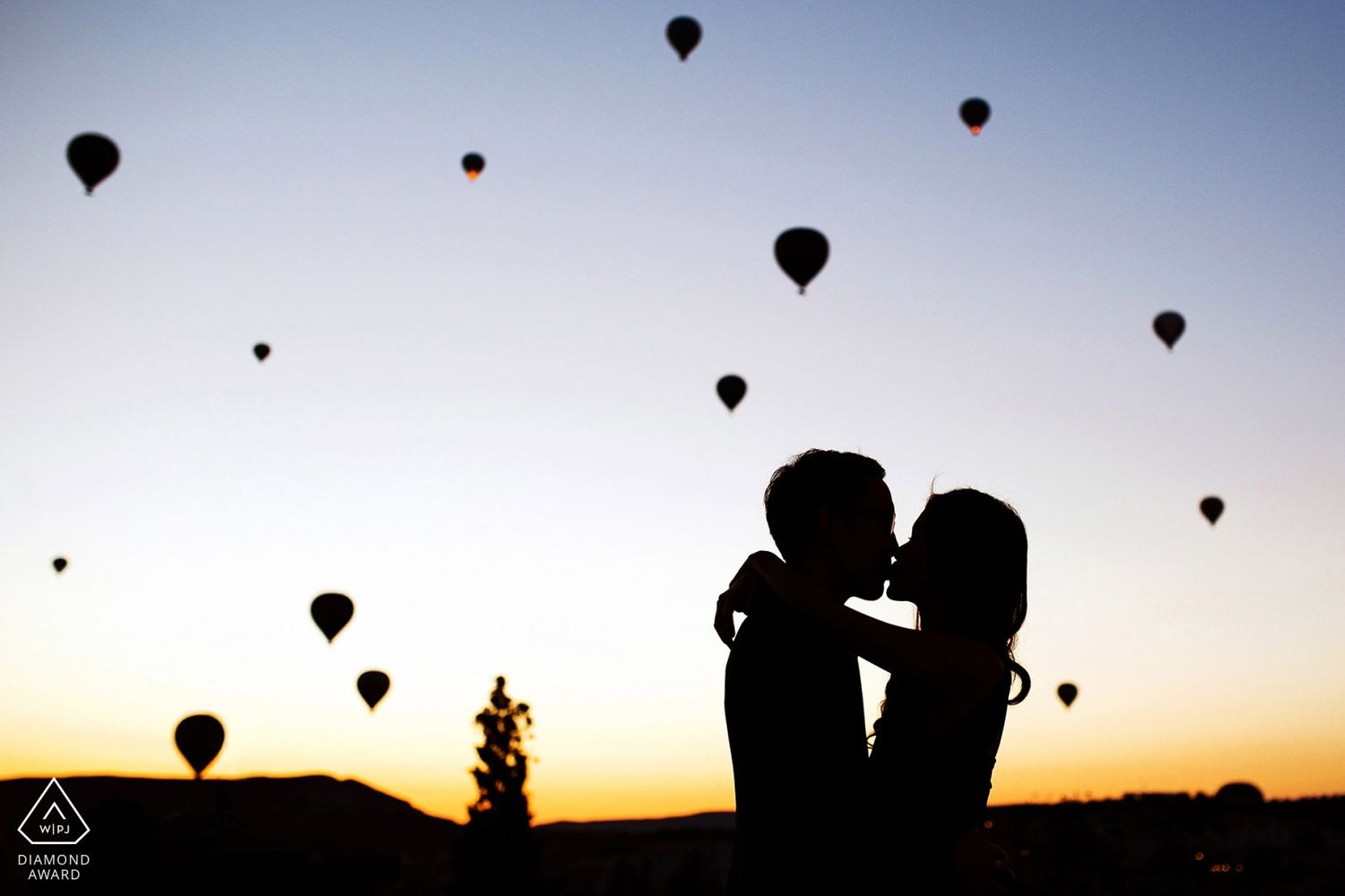WPJA Diamond Award-winning silhouette of an engaged couple kissing at sunrise, surrounded by hot air balloons in Cappadocia.