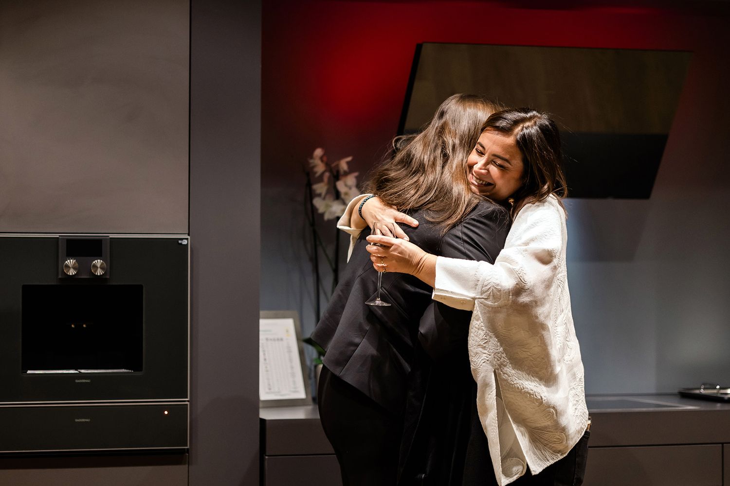 Two female executives sharing a warm, candid hug upon greeting each other at an upscale corporate networking event.