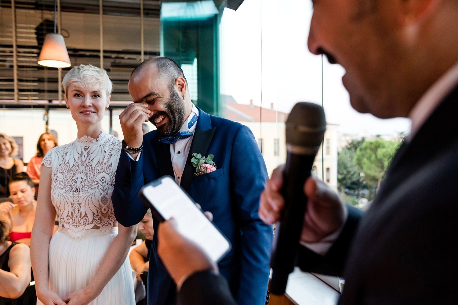 A groom wipes away tears of laughter next to his smiling bride during a funny wedding speech at Litera Restaurant in Istanbul.