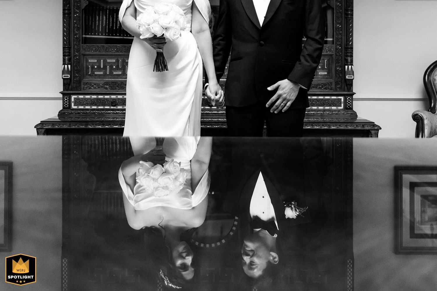 WPJA award-winning creative wedding photo featuring a reflection of a smiling bride and groom in a dark, polished wooden table.