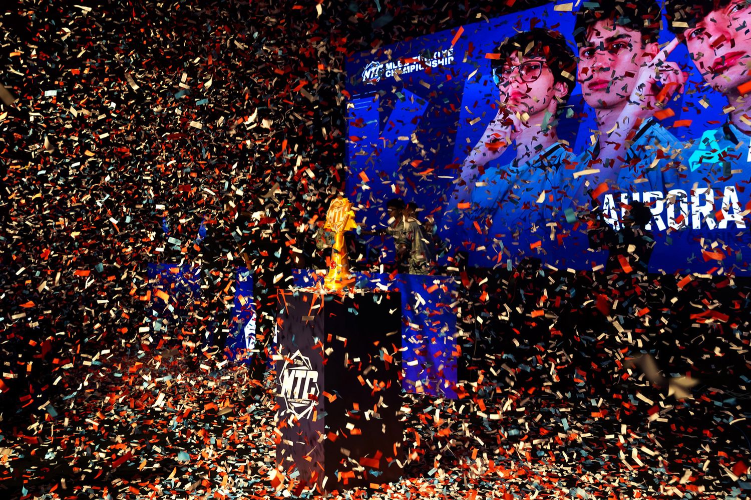 A golden championship trophy surrounded by a massive explosion of colorful confetti on the main stage of an esports tournament.